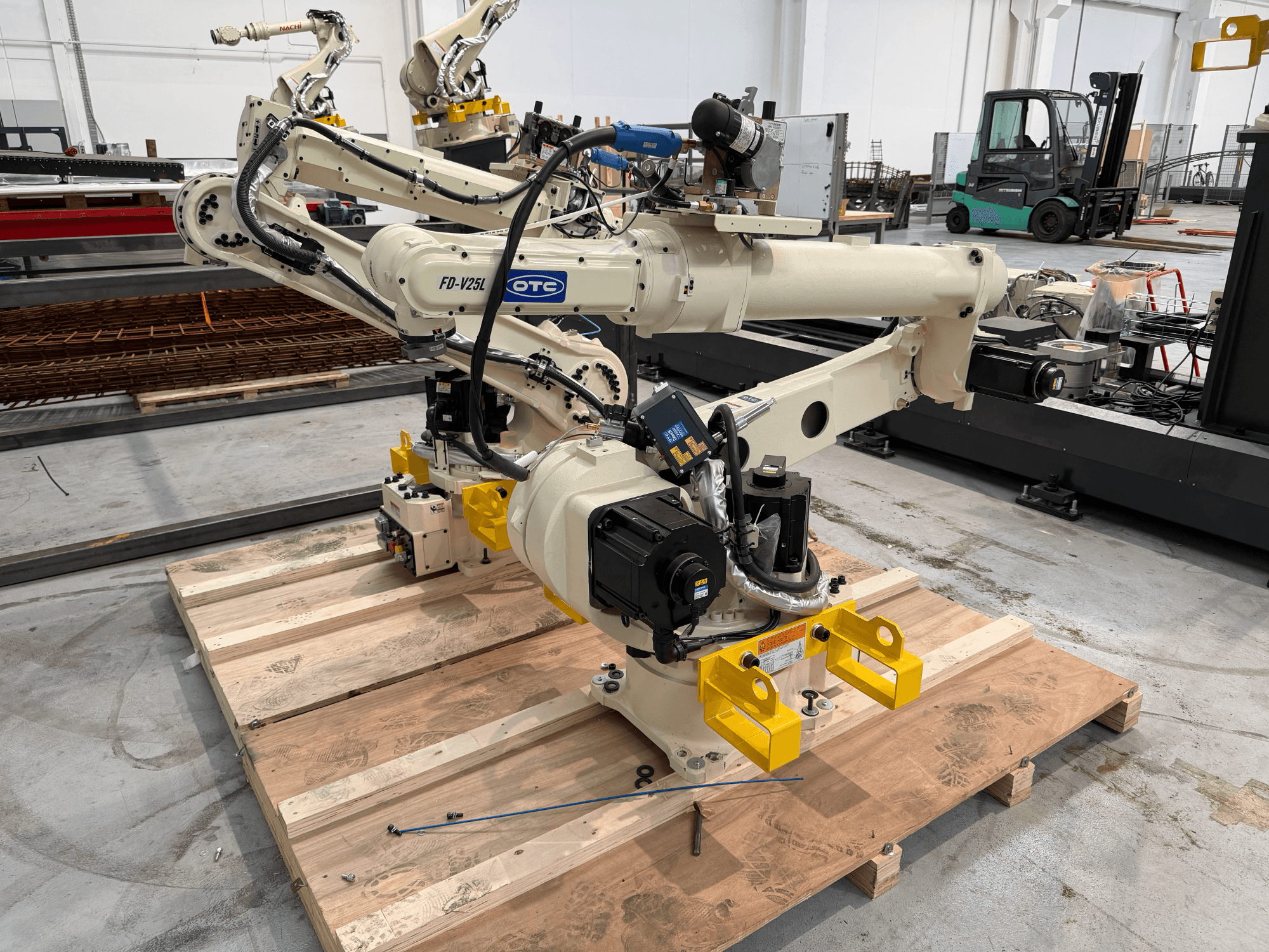OTC Daihen FD19-V25L robot kolunun önden görünümü; sarı renkli tutucu pençeleri ve ahşap palet üzerinde açıkta görünen mekanik bileşenleri ile.