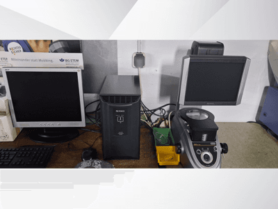 Biri Acer diğeri Keyence olmak üzere iki bilgisayar monitörü, siyah bir cihazın yanında ve önden bakıldığında bir mikroskop.