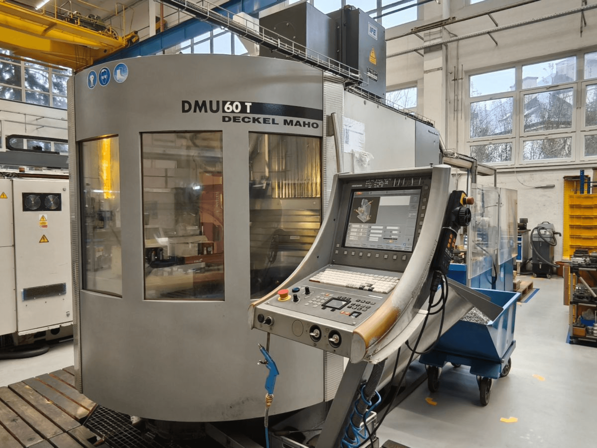 DECKEL MAHO DMU 60T işleme merkezinin kontrol paneli ile dikey görünümü, bir atölye içinde hassas takımları gösterir.