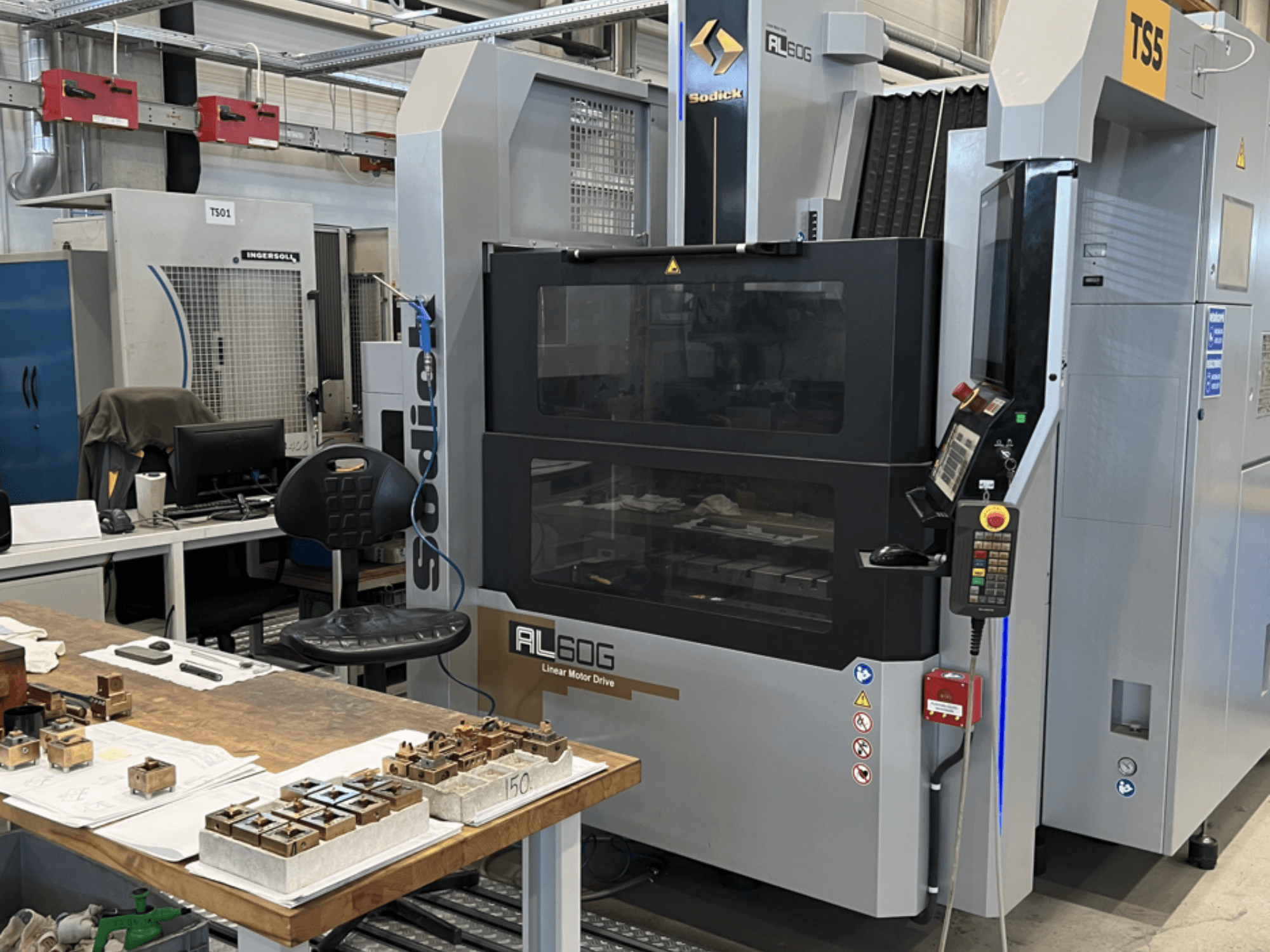 Sodick AL60G Die-Sinking EDM Makinesi; kontrolleri, pencereyi ve çeşitli metal parçaların bulunduğu çalışma alanını gösteren önden görünüm.