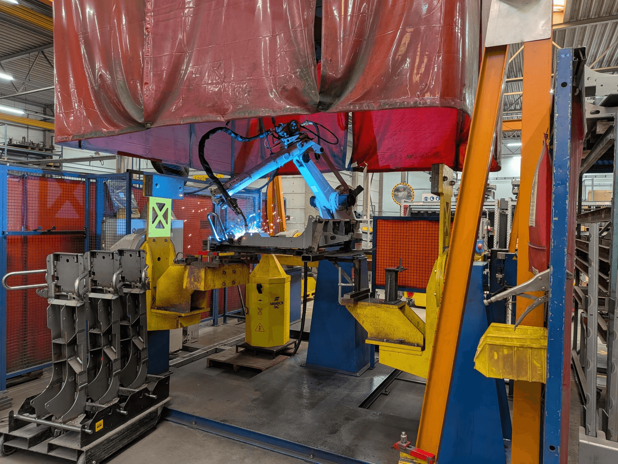 OTC Daihen DR4200 kaynak robotu, önden bakıldığında, parlak mavi kaynak arkı ve koruyucu kapağıyla birlikte çalışırken.