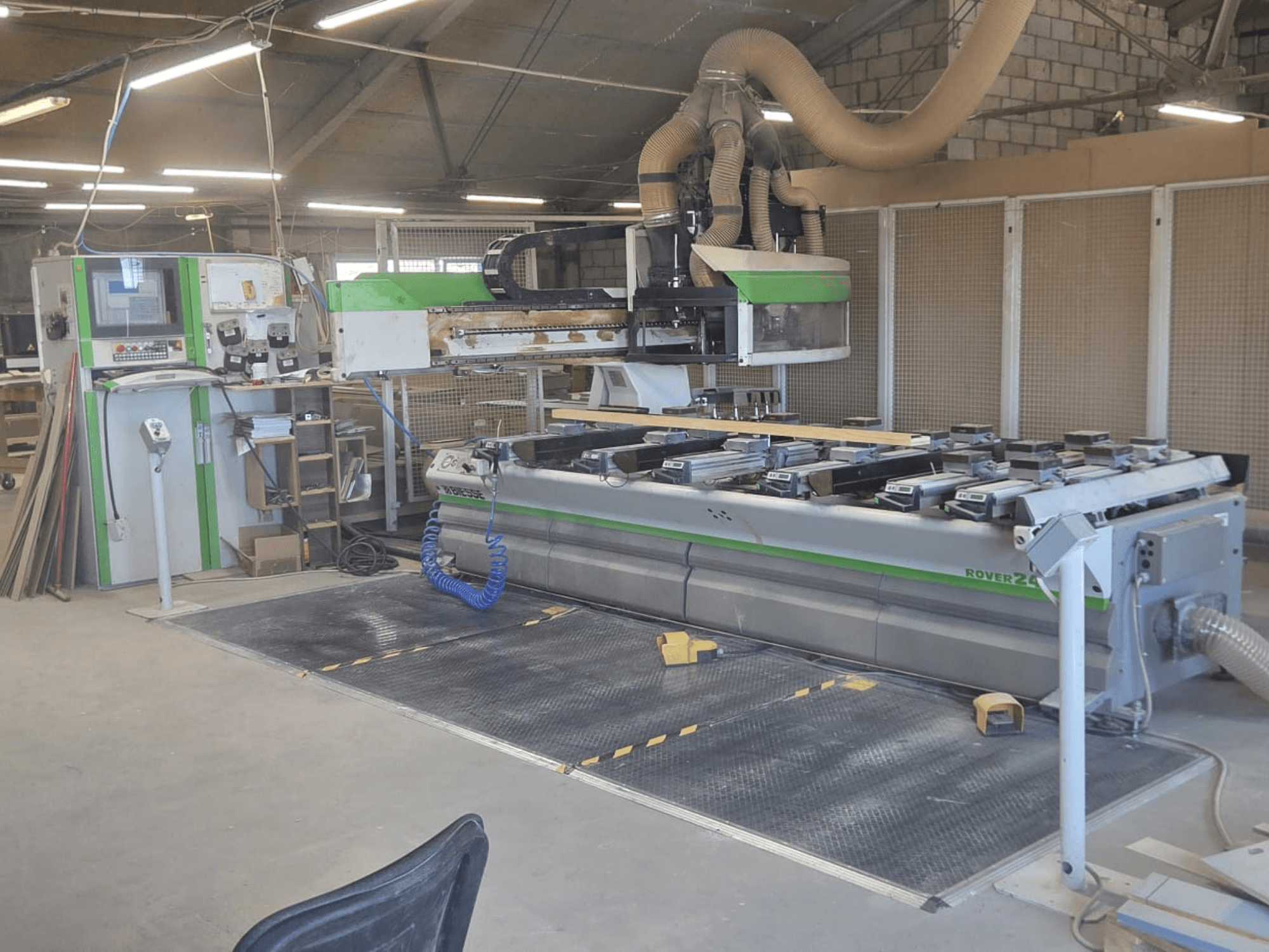CNC İşleme Merkezi BIESSE Rover 24S, kontrol paneli ve ahşap parçalarla geniş çalışma yüzeyi bulunan bir atölyede.