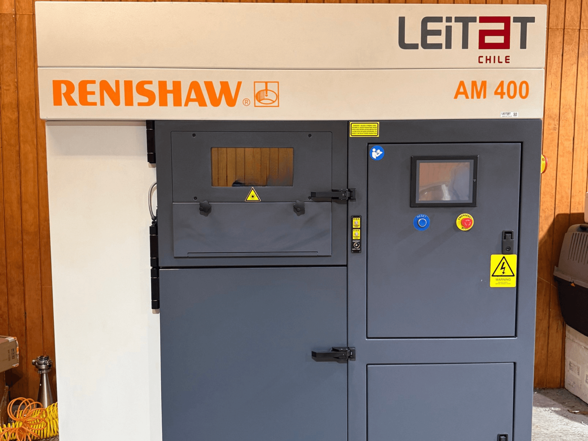 RENISHAW AM400 metal 3D yazıcının önden görünümü; kontrol paneli, uyarı etiketleri ve bakım erişim noktalarını göstermektedir.