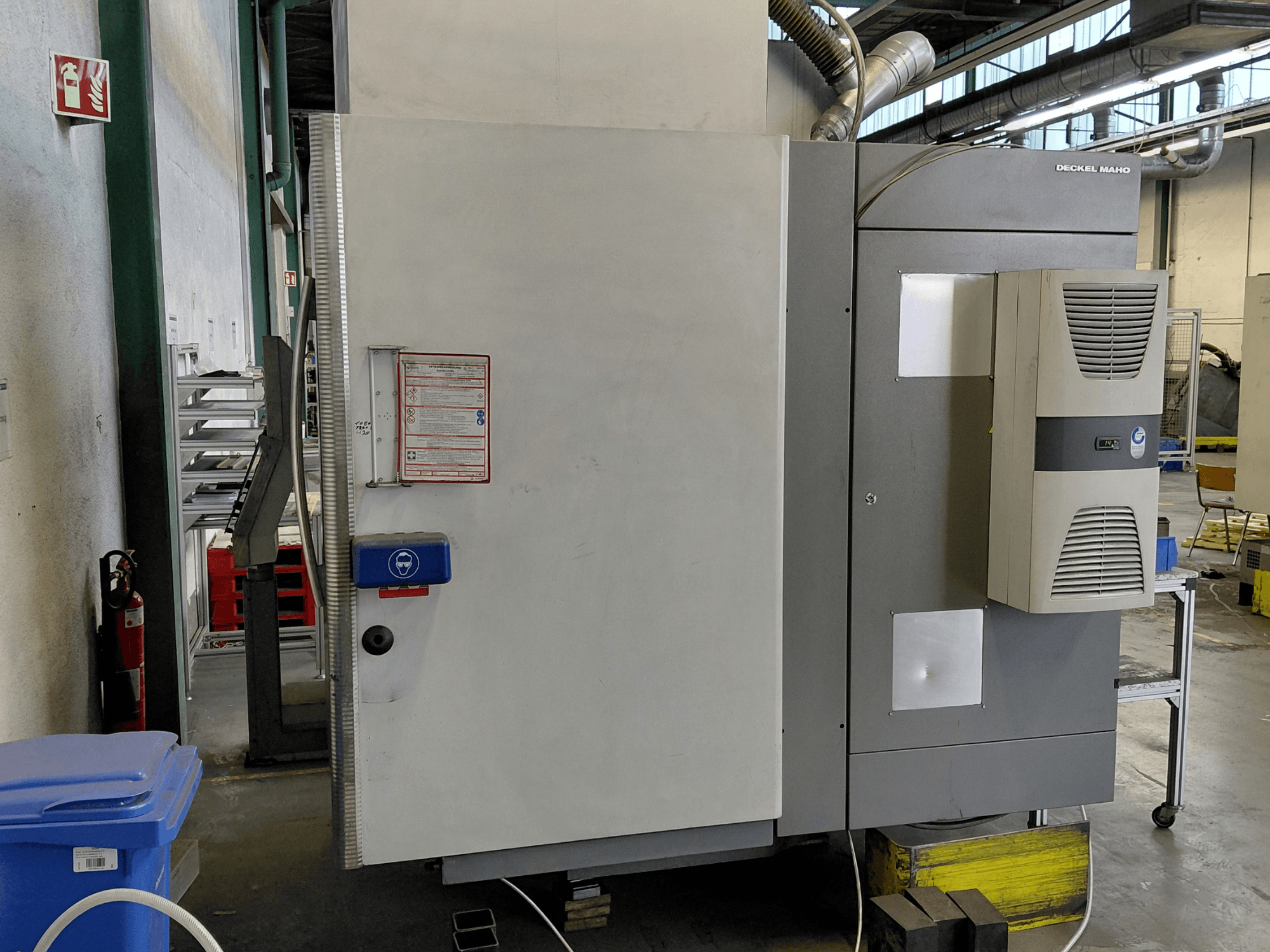 DECKEL MAHO DMC 635 V dikey işleme merkezinin kontrol paneli ve güvenlik etiketleri görünür şekilde yandan görünümü.