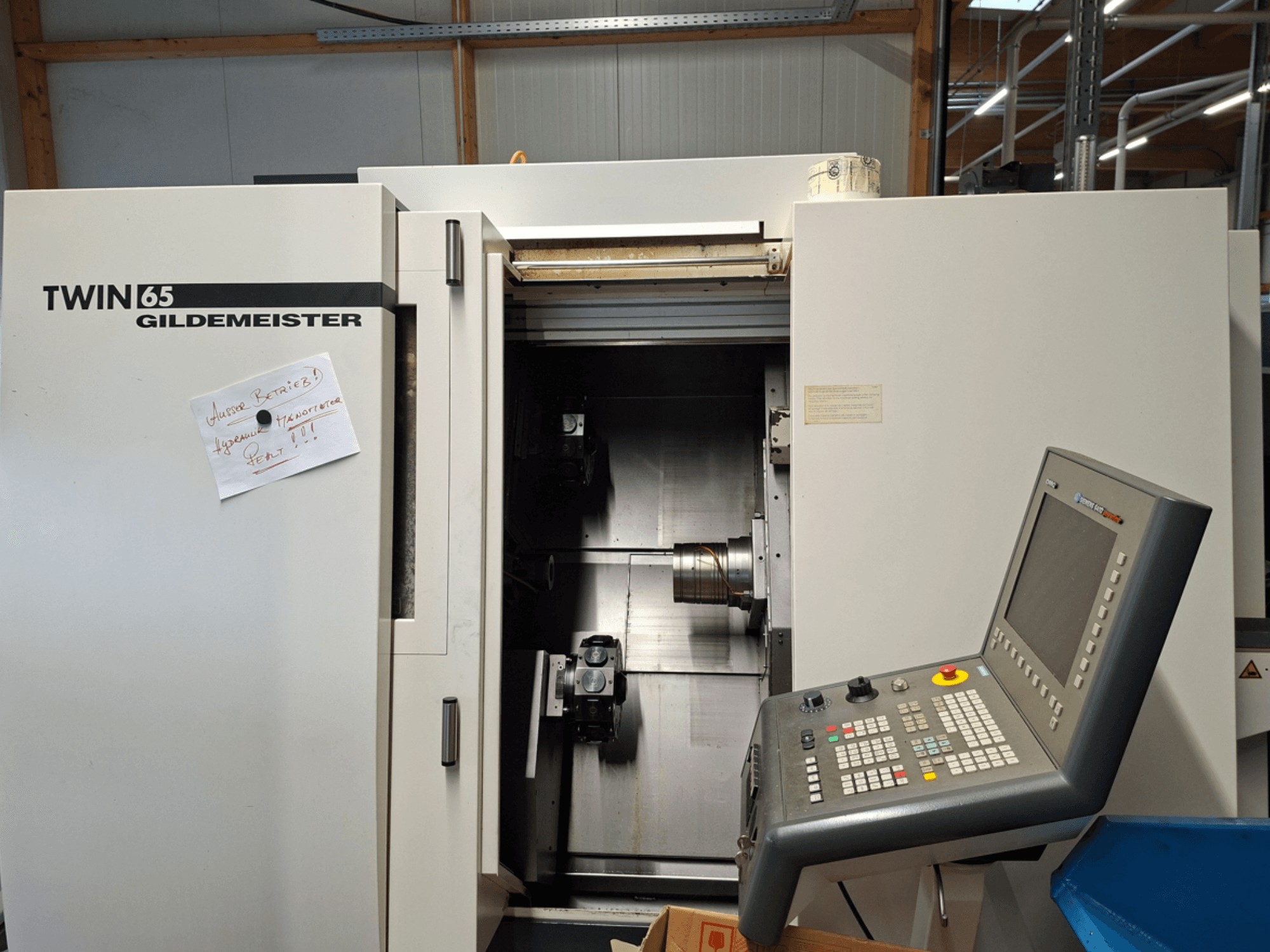 Gildemeister TWIN 65 CNC torna tezgahı, kontrol panelini gösteren önden görünüm ve görünür makinelerle kısmen açık hazne.