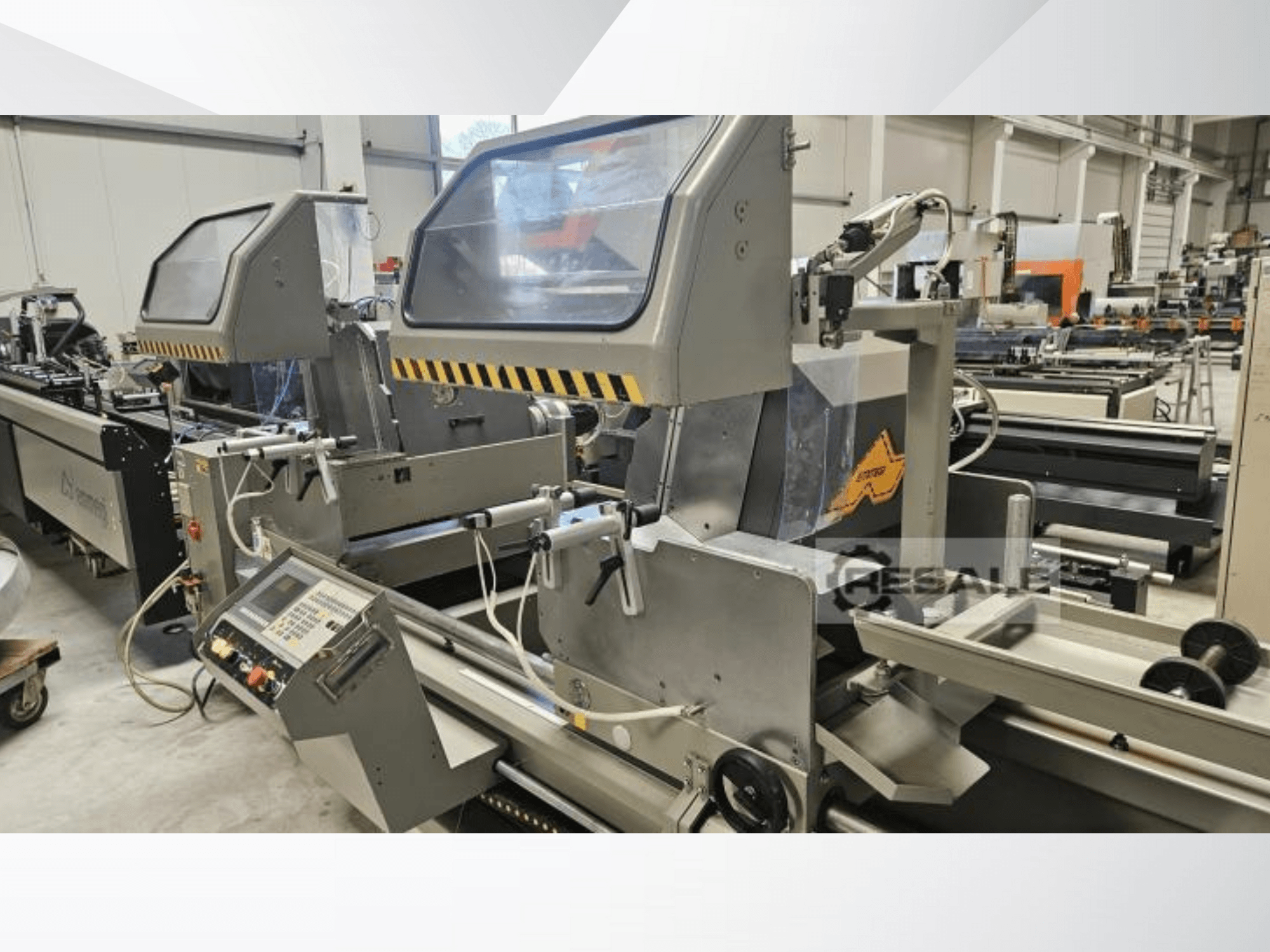 Fabrika ortamında çift testere makineleri; kontrol panelini, cam kapakları ve kesme bileşenlerini gösteren önden görünüm.