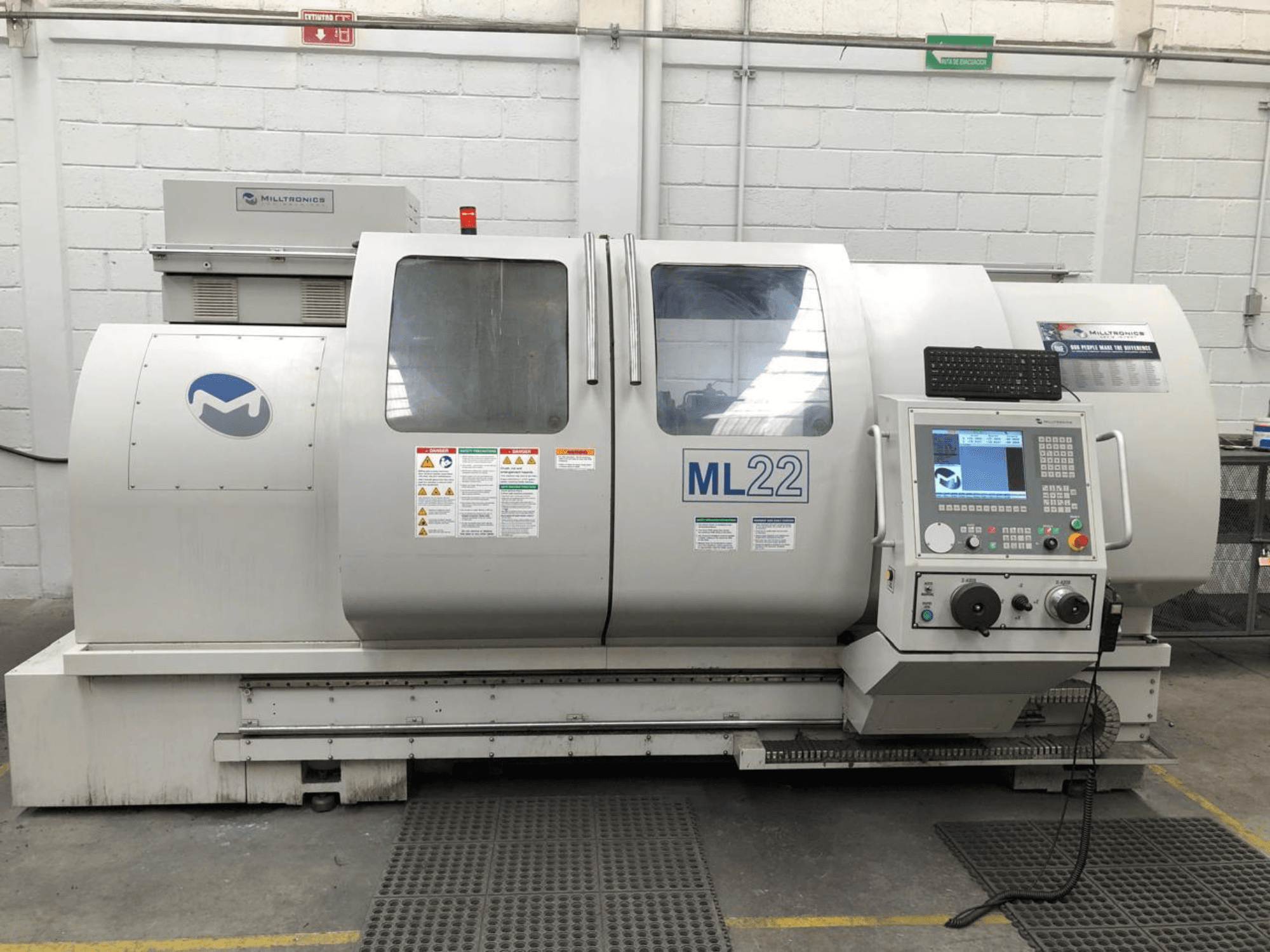 Dikey İşleme Merkezi MILLTRONICS RH 20, kontrol panelini, marka logosunu ve makine üzerindeki güvenlik etiketlerini gösteren önden görünüm.