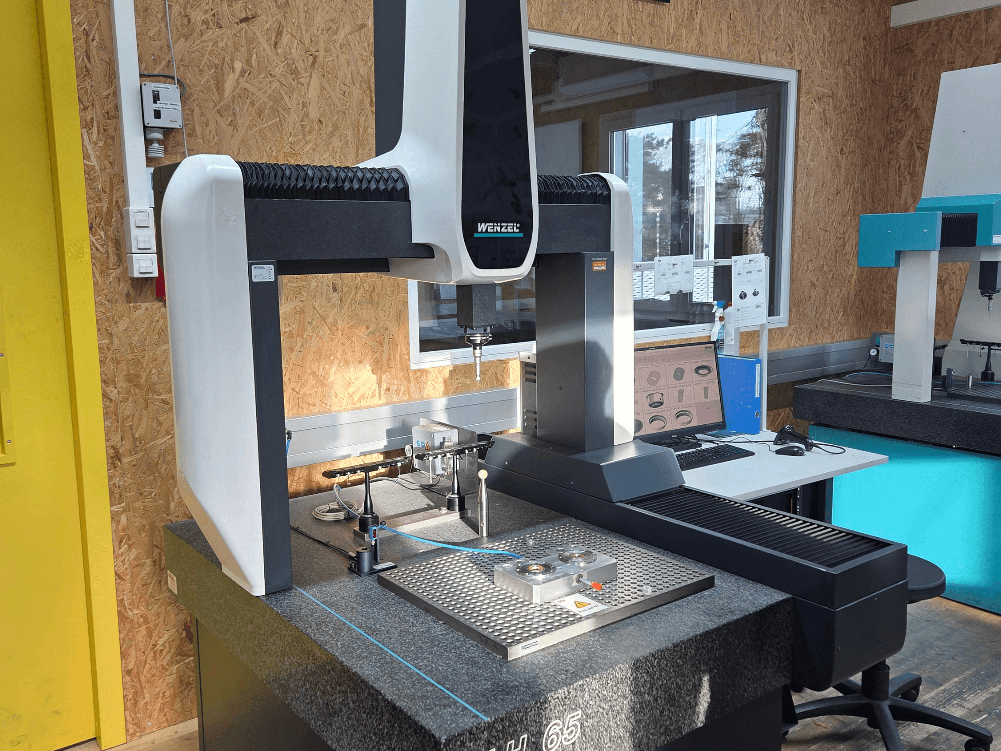 Wenzel LH 65 Koordinat Ölçüm Makinesi bir laboratuvar kurulumunda, önden görünüm, ölçüm araçlarını ve bir monitörü gösterir.