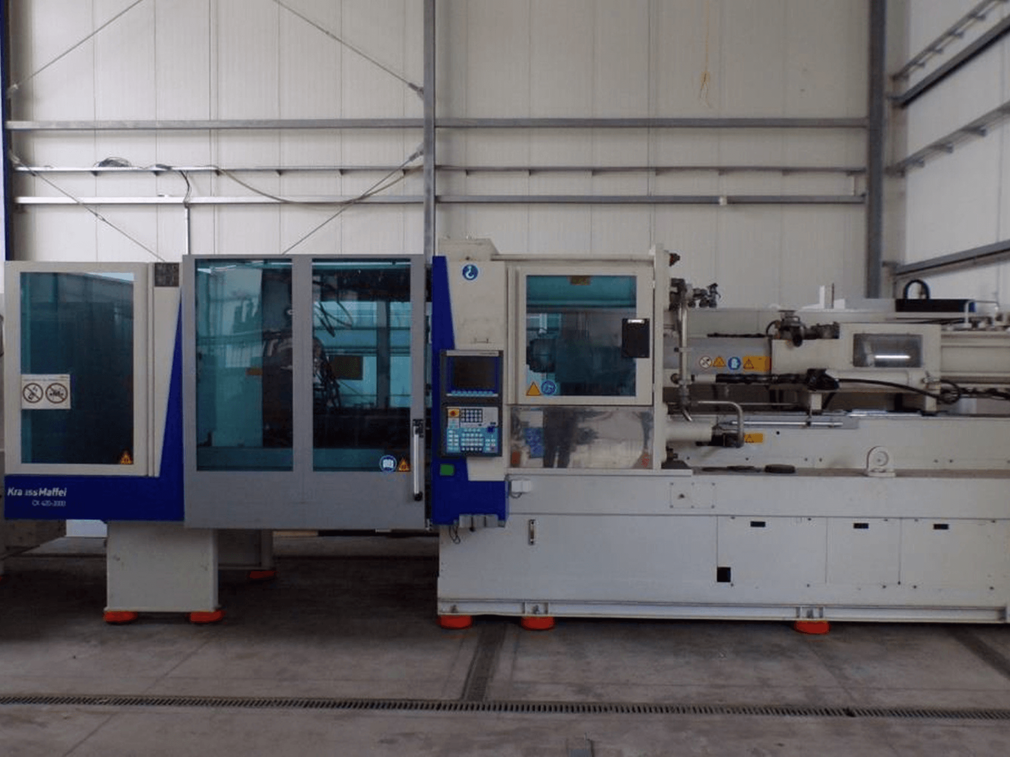 KraussMaffei enjeksiyon kalıplama makinesi, yandan görünüm, kontrol paneli ve güvenlik göstergeleri, fabrika ortamında görülebilir.