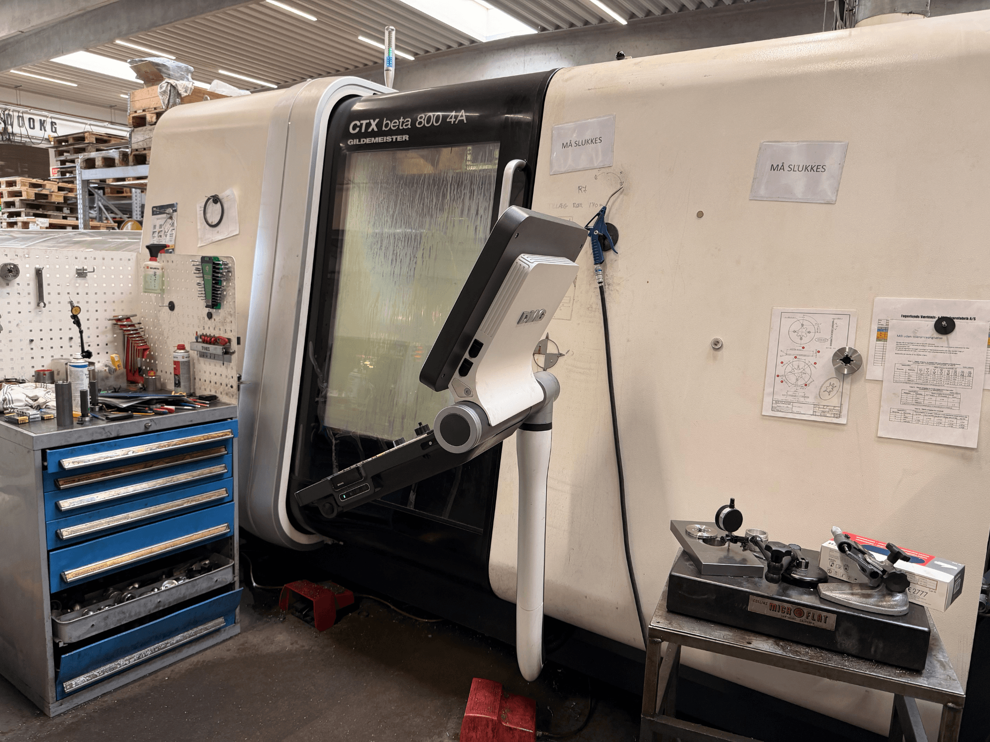 Bir atölyede DMG MORI CTX Beta 800 4a dikey tornalama makinesi, yanında bir kontrol kolu ve teknik belgeler.
