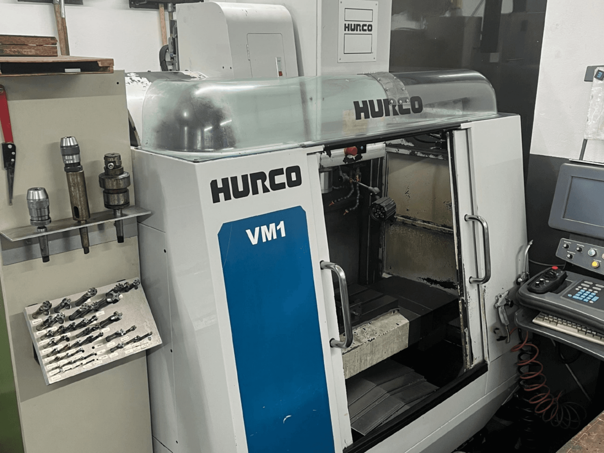 Hurco VM1 dikey işleme merkezi önden görünüm, şeffaf bir kapak, kontrol paneli ve monte edilmiş takımlar.