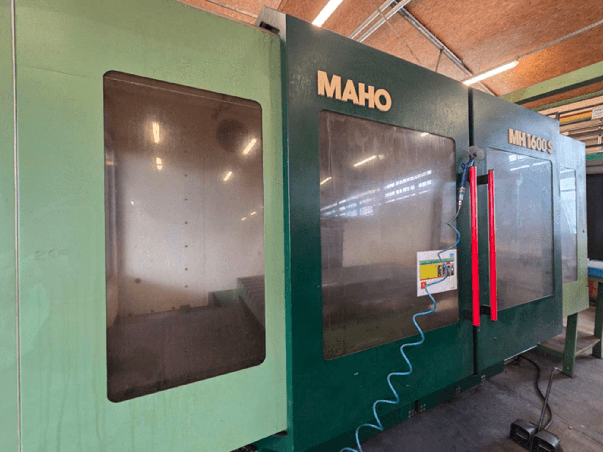 MAHO 1600S Üniversal İşleme Merkezi'nin önden görünümü, çift şeffaf panel ve kırmızı tutamaklı kontrol paneline sahiptir.