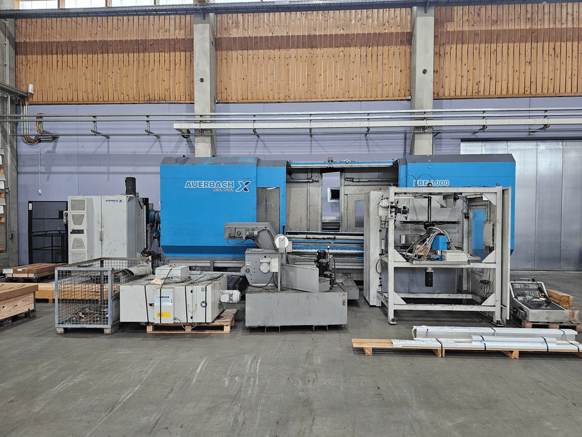 Fabrika ortamında Auerbach X LBF-3000 makinesi, yandan görünüm, görünür kontrol paneli ile gri ve mavi bileşenlere sahip.