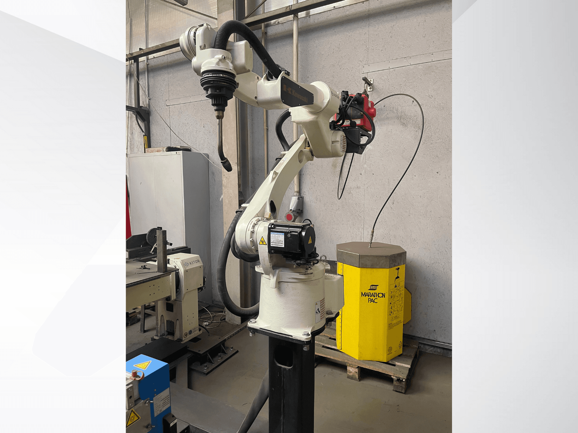 Kawasaki robotik kolun yandan görünümü, monte edilmiş bir takım tutucu ve arka planda sarı bir güç ünitesi.