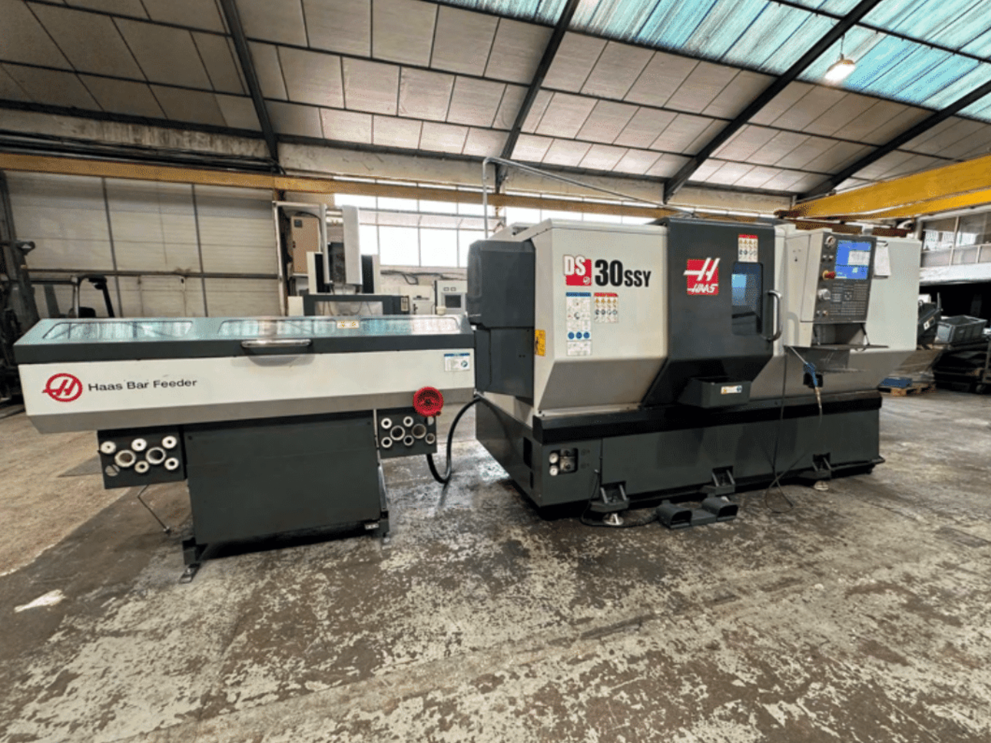 Haas Çubuk Besleyicili Haas DS-30SSY CNC torna tezgahı, atölye ortamında kontrol paneli ve besleme mekanizmasını gösteren yandan görünüm.