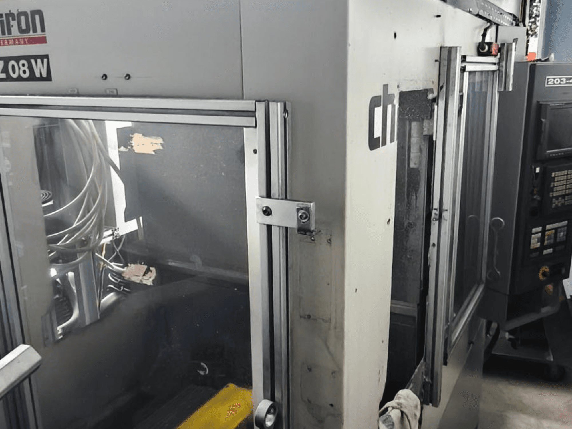 Dikey İşleme Merkezi CHIRON FZ 08 W, kontrol panelini ve kısmen açık kapıları gösteren önden görünüm, görünür iç bileşenler.