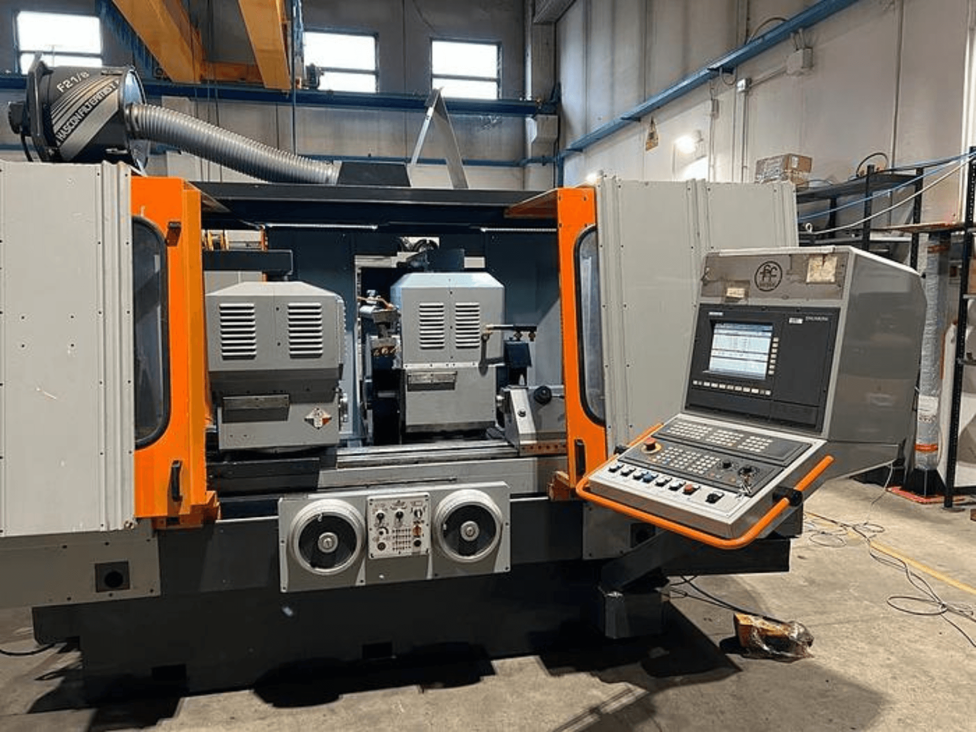 Çift iş mili, kontrol paneli ve turuncu vurgulara sahip bir CNC makinesinin önden görünümü. Havalandırma kanalı ve operasyonel kontrollere sahiptir.