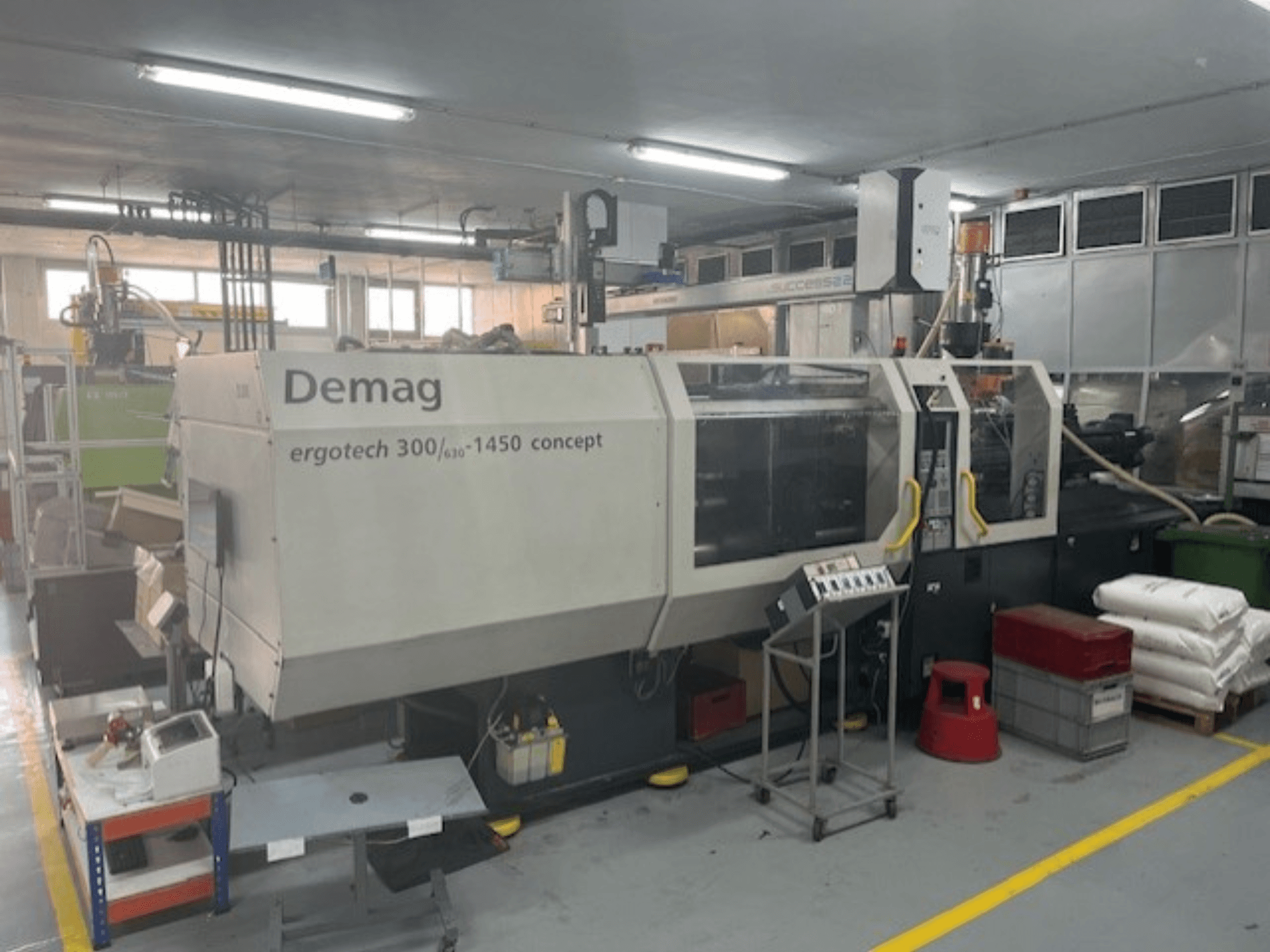 Demag ERGOTECH CONCEPT 3000-1450 hidrolik enjeksiyon kalıplama makinesi, önden görünüm, operasyonel kontroller ve yakındaki malzemeler ile.