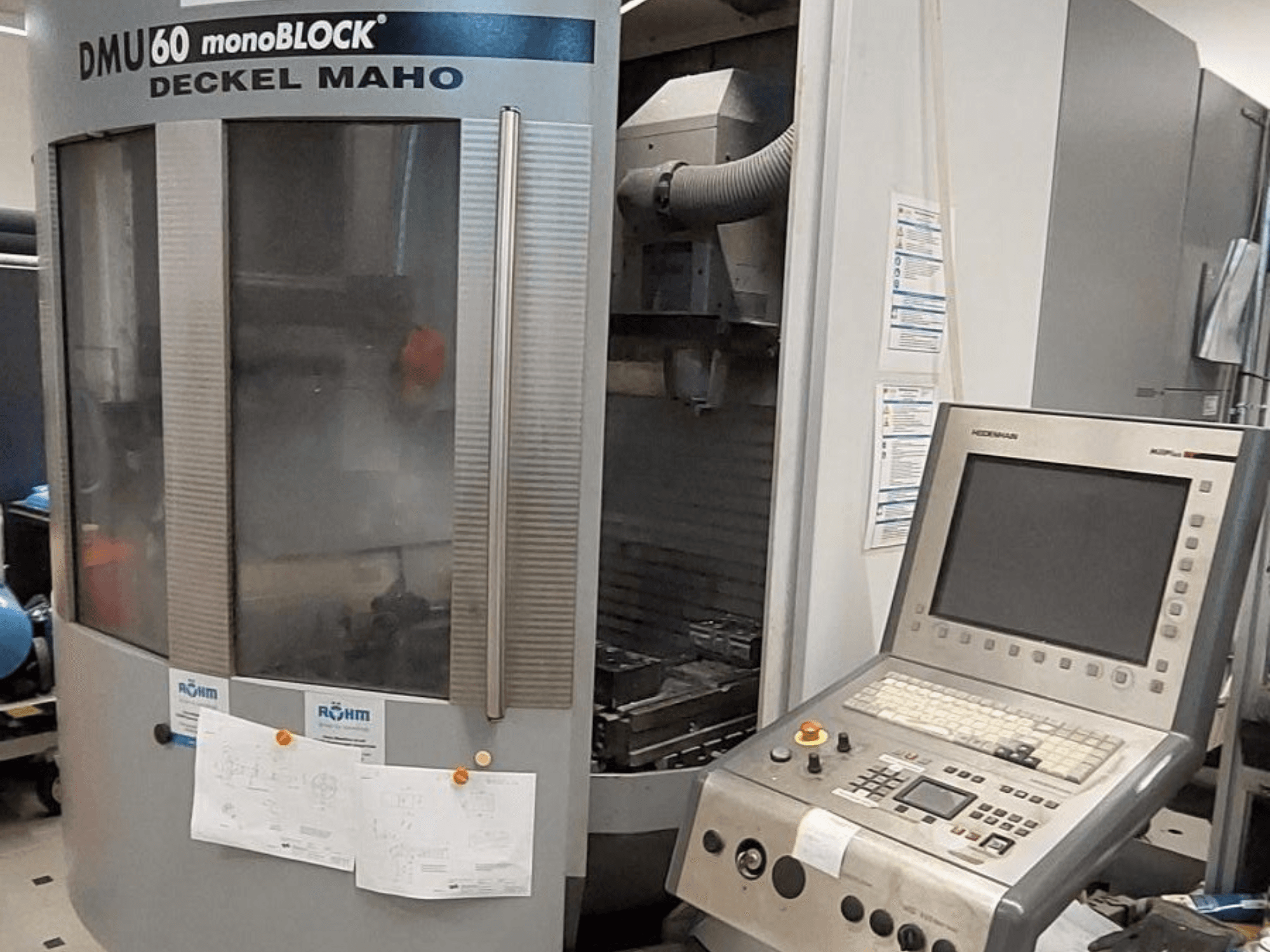 Deckel Maho'dan DMU 60 monoBLOCK, kontrol paneli ve teknik çizimleri eklenmiş bir CNC freze makinesinin önden görünümü.