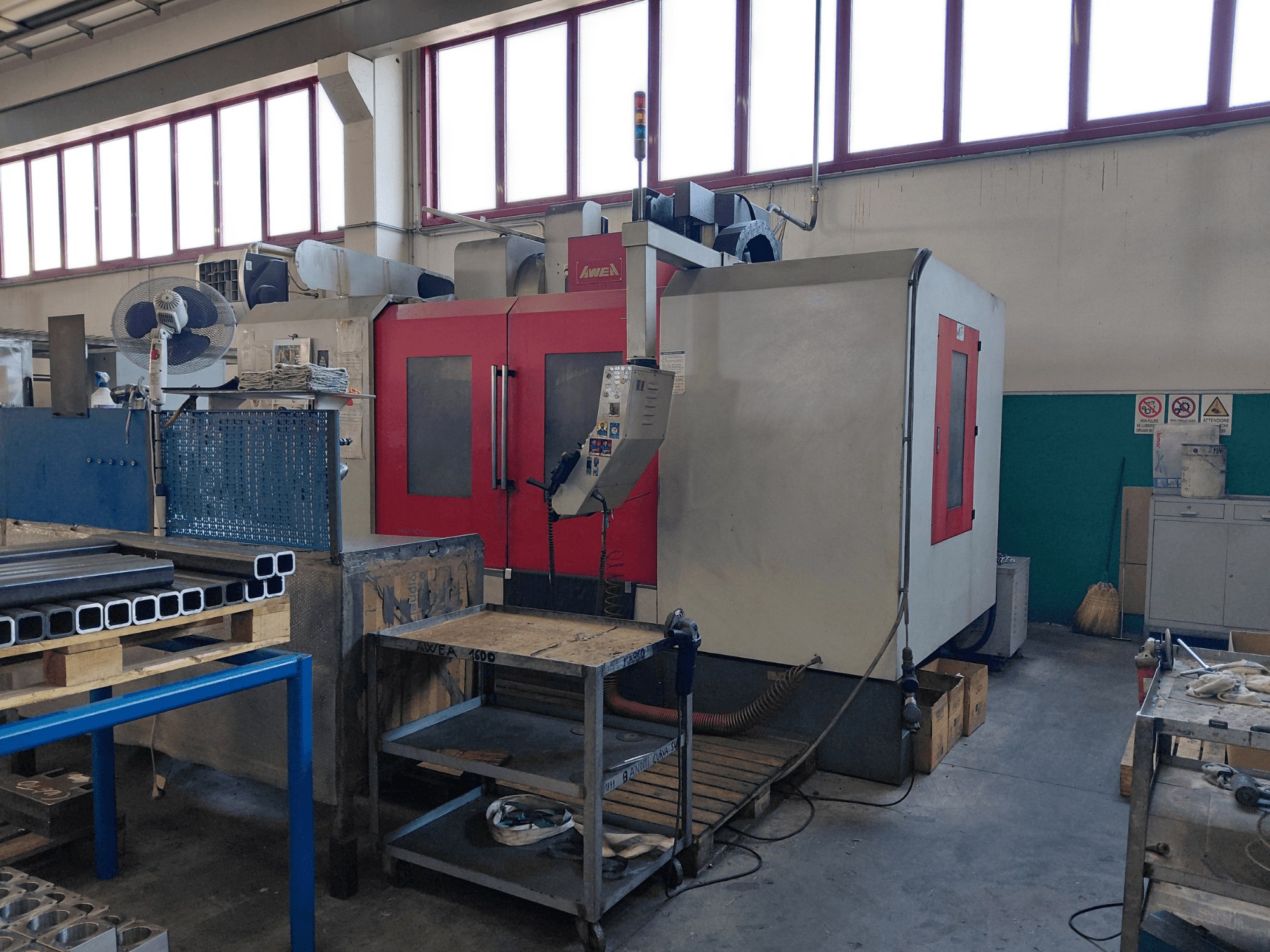 AWEA BM-1600 dikey işleme merkezi, önden görünüm; kırmızı ve gri gövdeli; yakınında iş tezgahı ve aletler görülüyor.