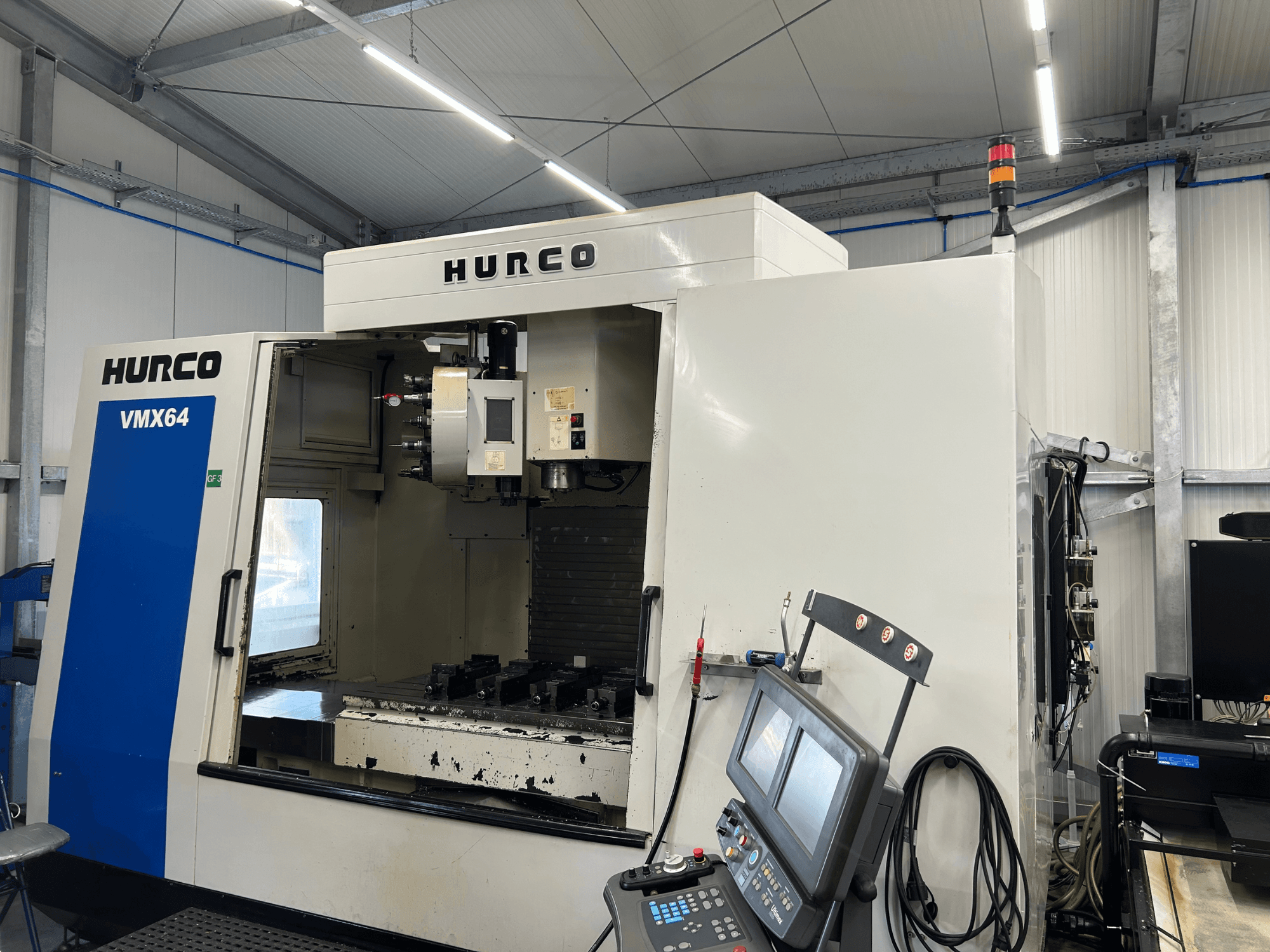 Hurco VMX 64 dikey işleme merkezi, önden görünüm; kontrol paneli ve takımların bulunduğu açık çalışma alanı görülüyor.
