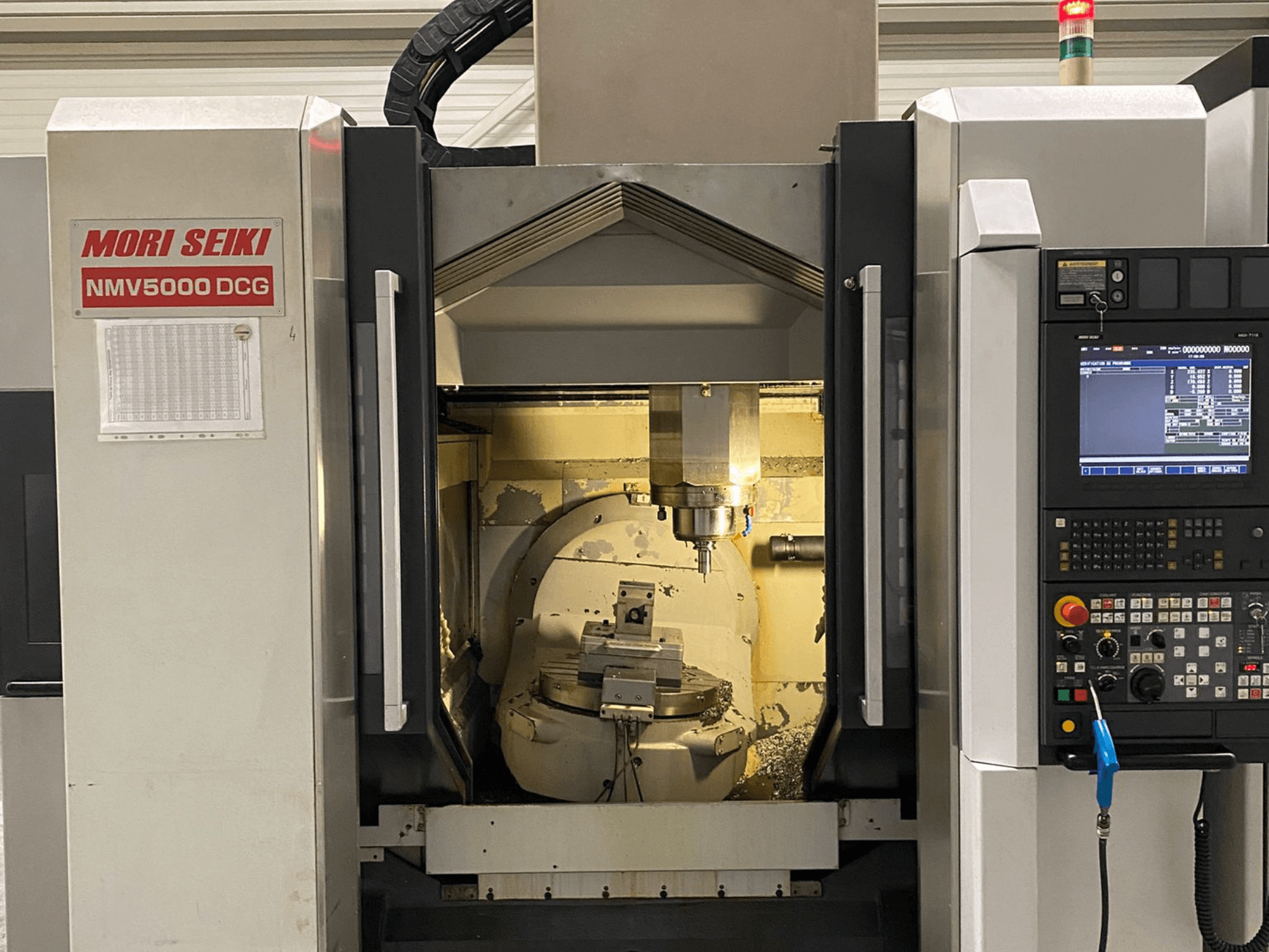MORI SEIKI NMV 5000DCG üniversal işleme merkezi, kontrol panelini ve iç işleme alanını gösteren önden görünüm.
