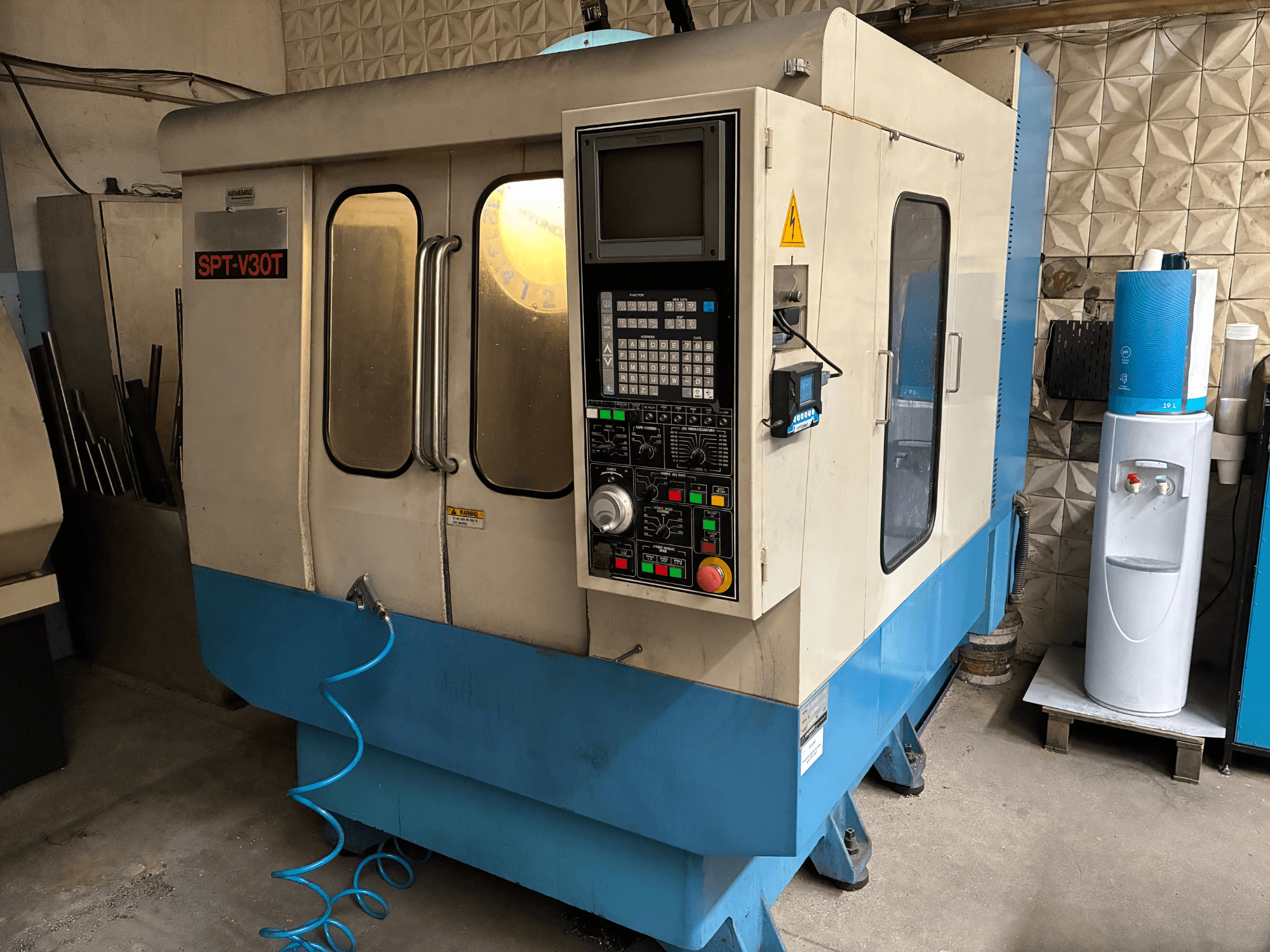 Mavi ve beyaz SPT-V30T CNC makinesi, kontrol paneli, kapılar ve hava hortumunu gösteren önden görünüm. Hassas işleme için mükemmeldir.