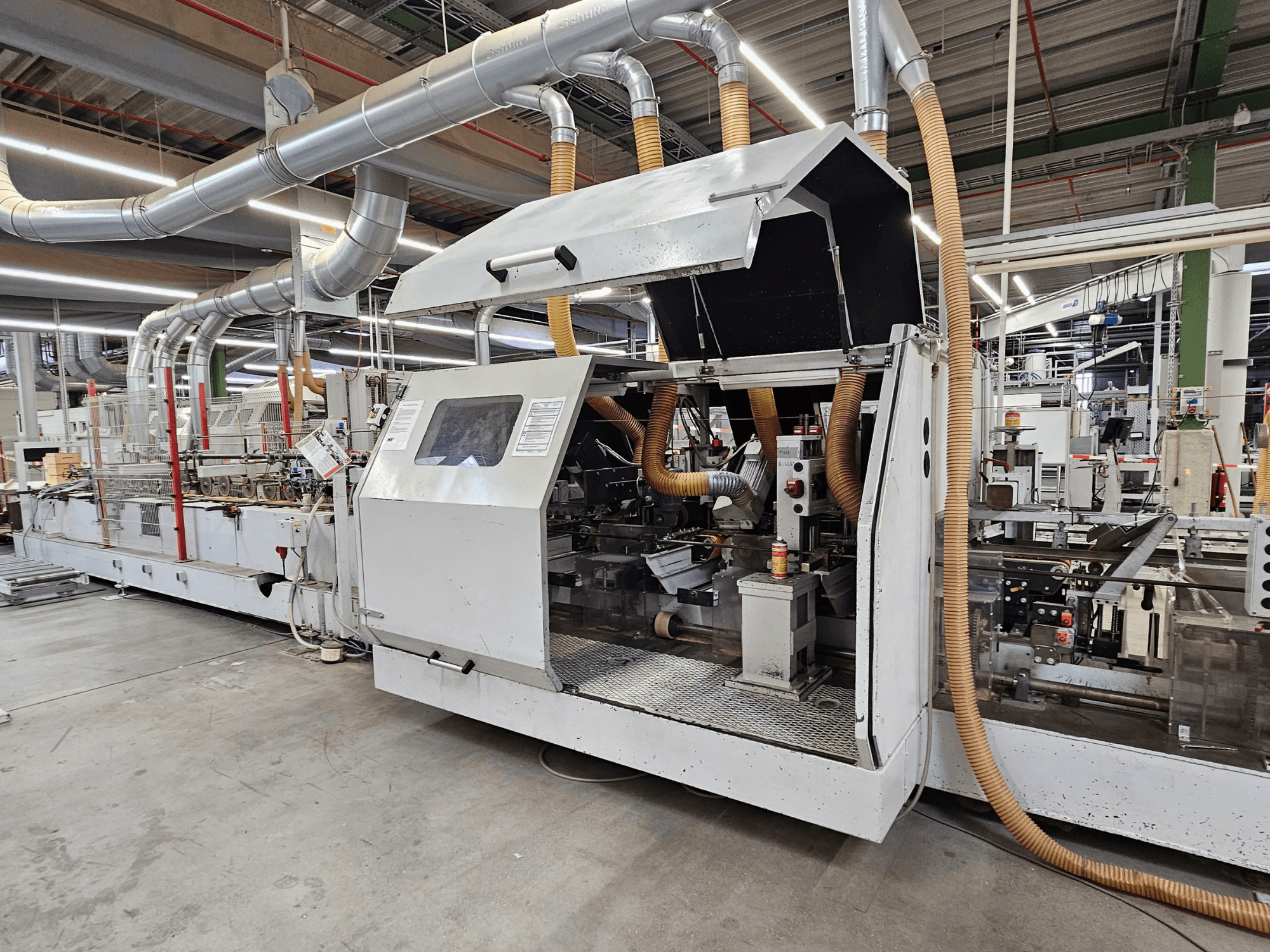 Fabrika ortamında HOMAG FG63 kenar bantlama makinesi, operasyonel bileşenleri ve toz emme sistemini gösteren yandan görünüm.