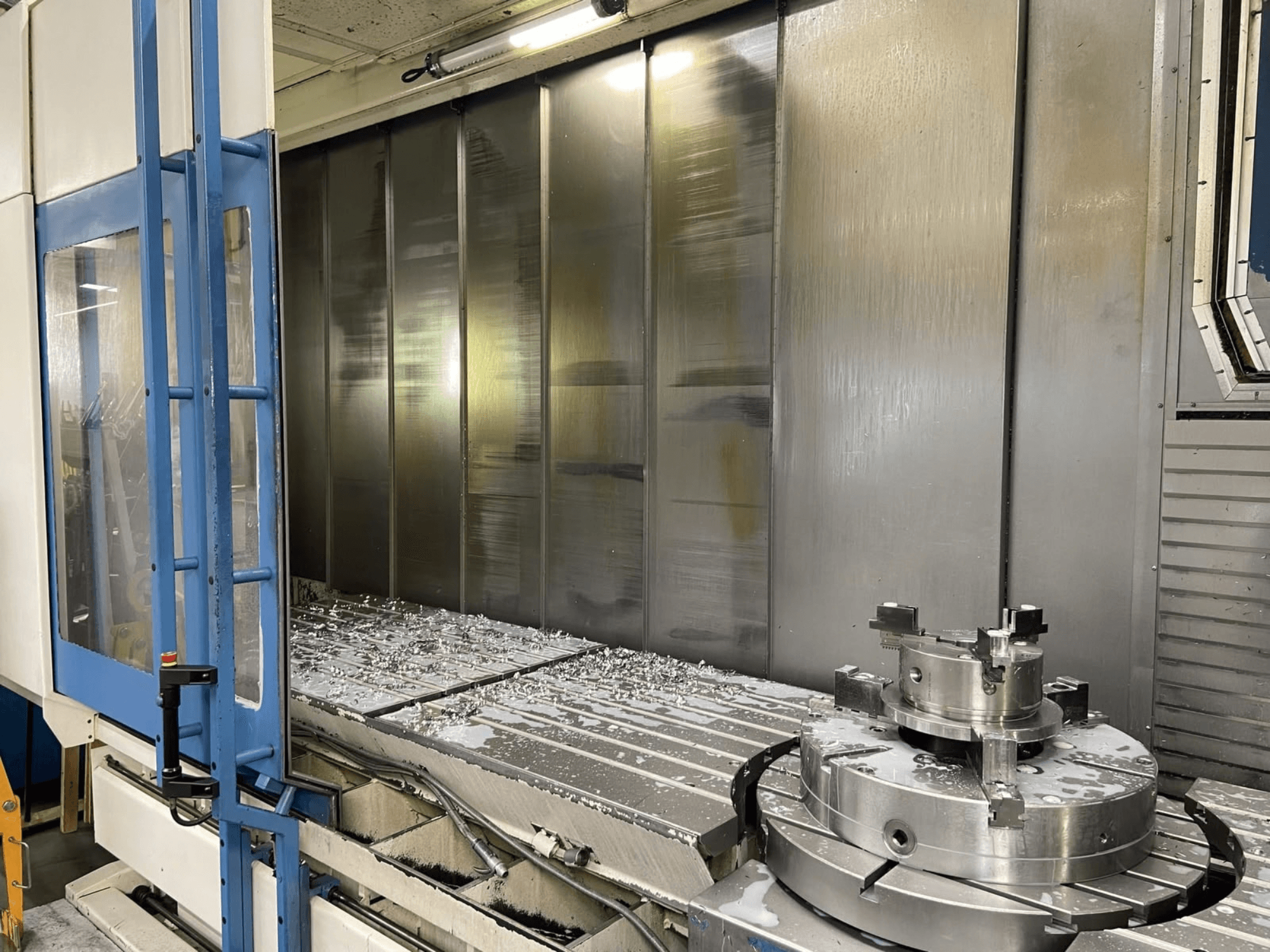 AXA VHC-3-3000-M/E dikey işleme merkezi, önden görünüm; iş masası üzerinde frezelenmiş metal talaşları ve kesici aletler görülmektedir.