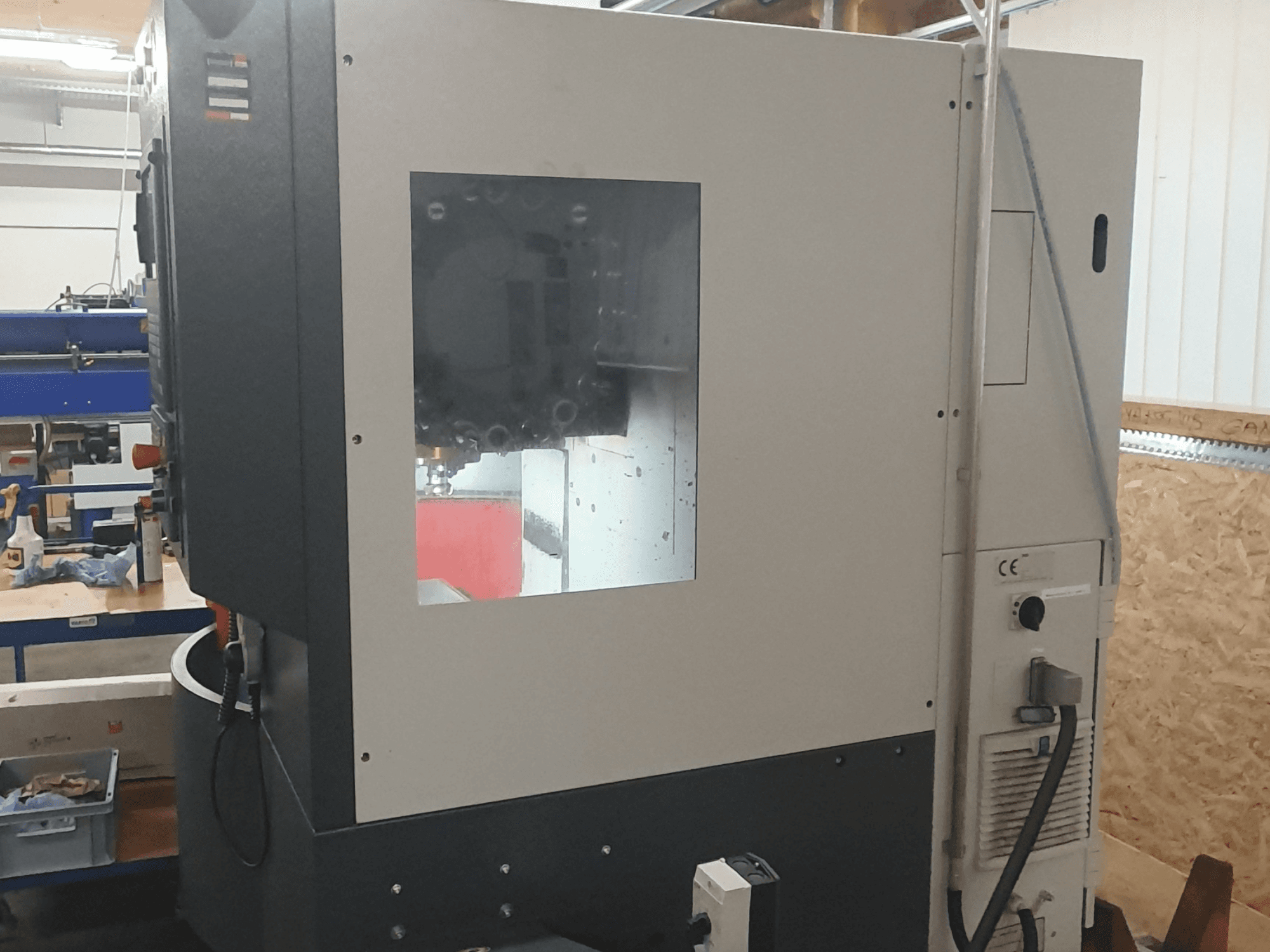 Görünür kontrol paneli, geniş izleme penceresi ve karmaşık iç bileşenleri ile bir metal işleme makinesinin yandan görünümü.