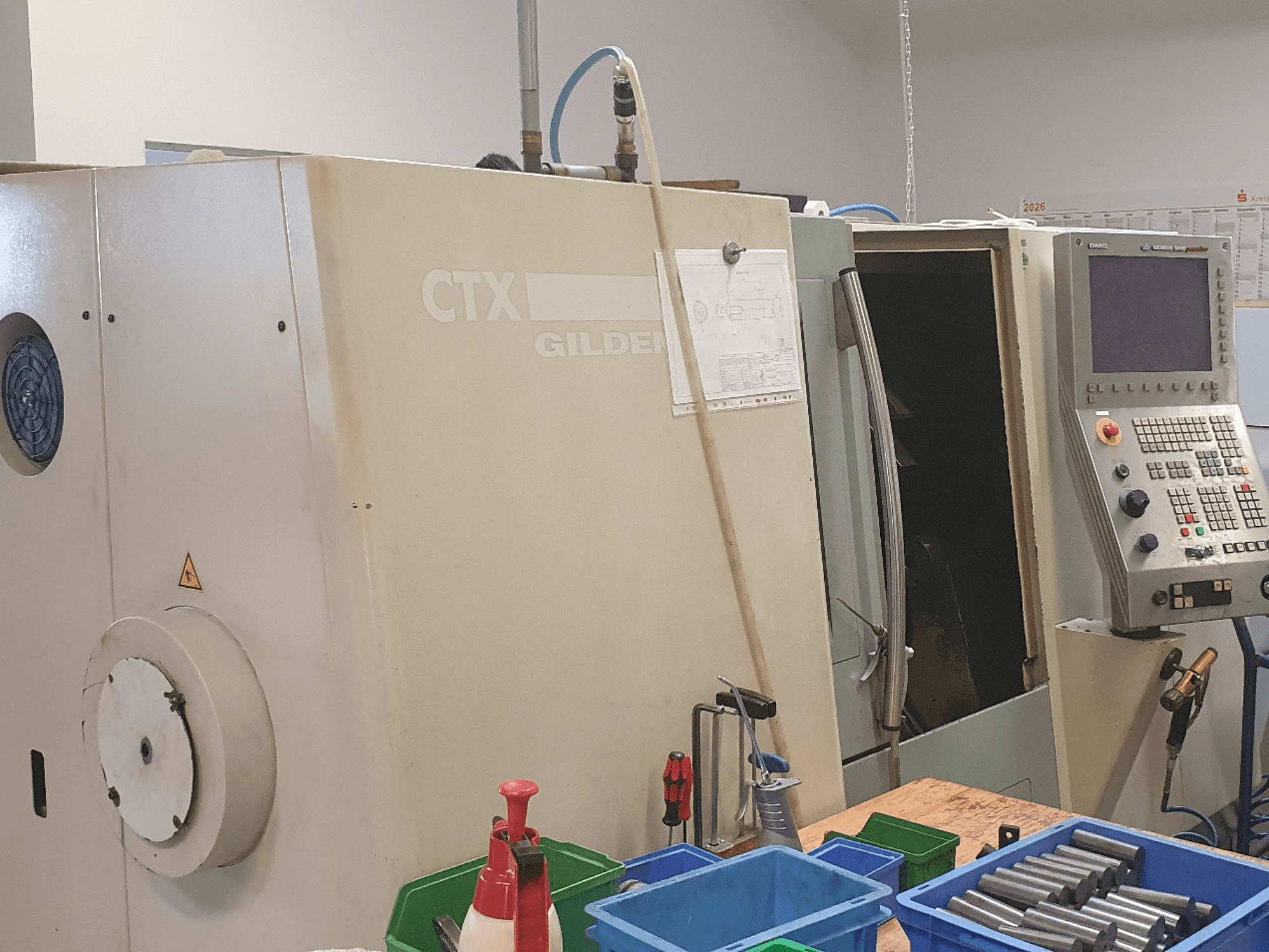 DMG GILDEMEISTER CTX 310 yatay torna tezgahının önden görünümü; kontrol paneli görünüyor, ön planda aletler ve kaplar yer alıyor.