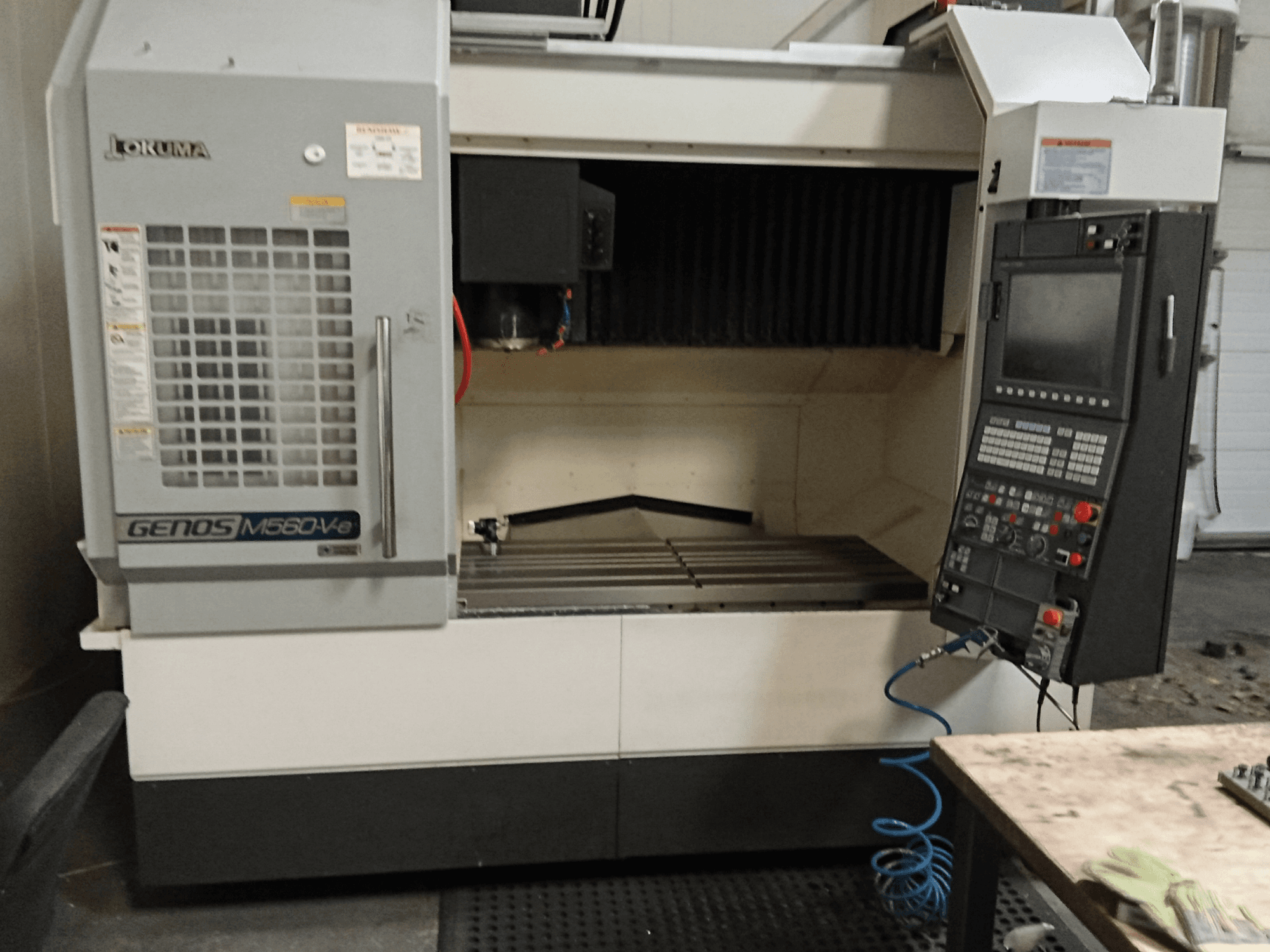 Okuma GENOS M560-V, kontrol paneli, CNC arayüzü ve görünür kesme alanı ile dikey işleme merkezinin önden görünümü.