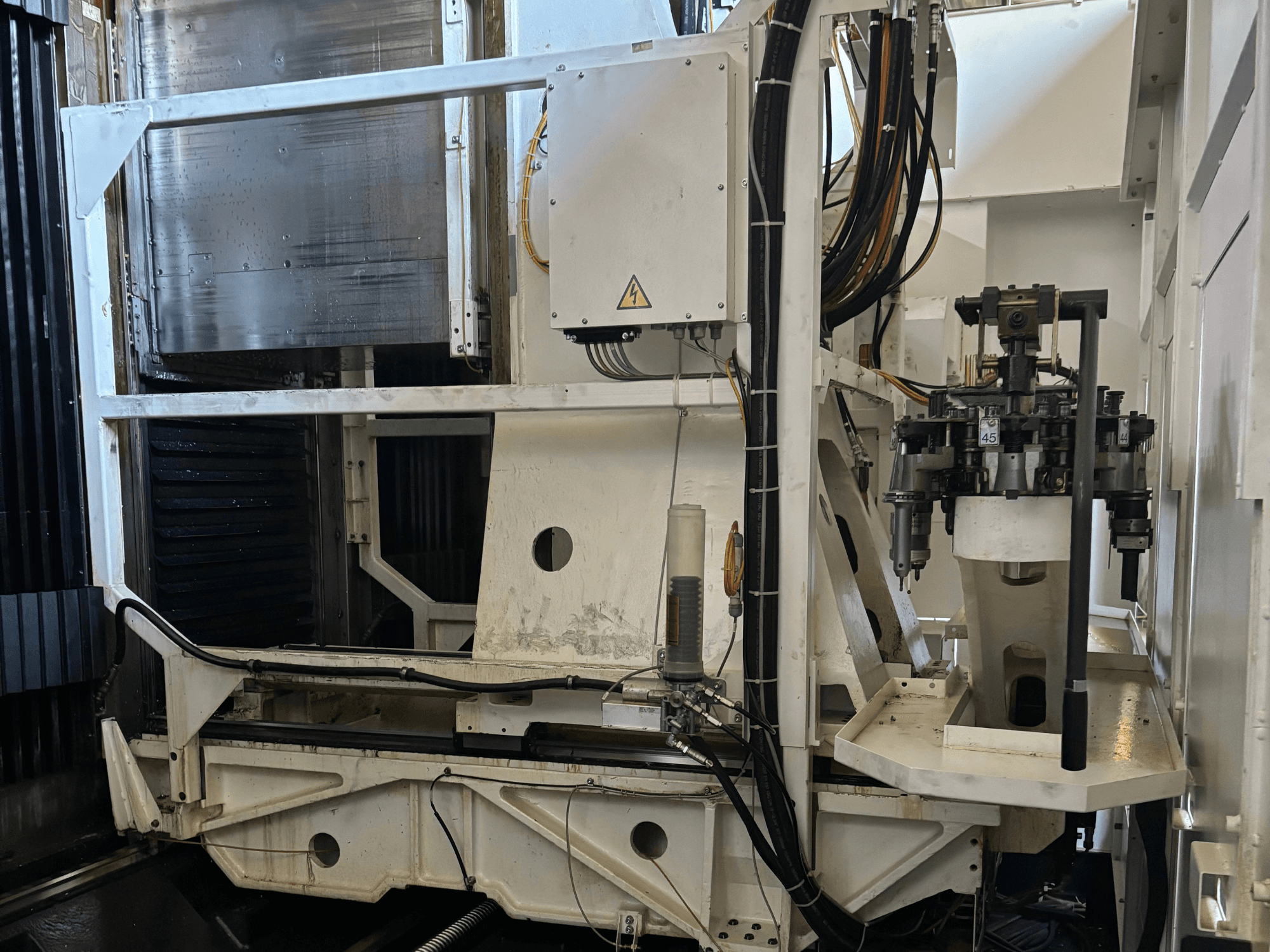 Görünür aletler, borular ve kontrol paneli ile beyaz bir CNC freze makinesini gösteren endüstriyel makine yan görünümü.