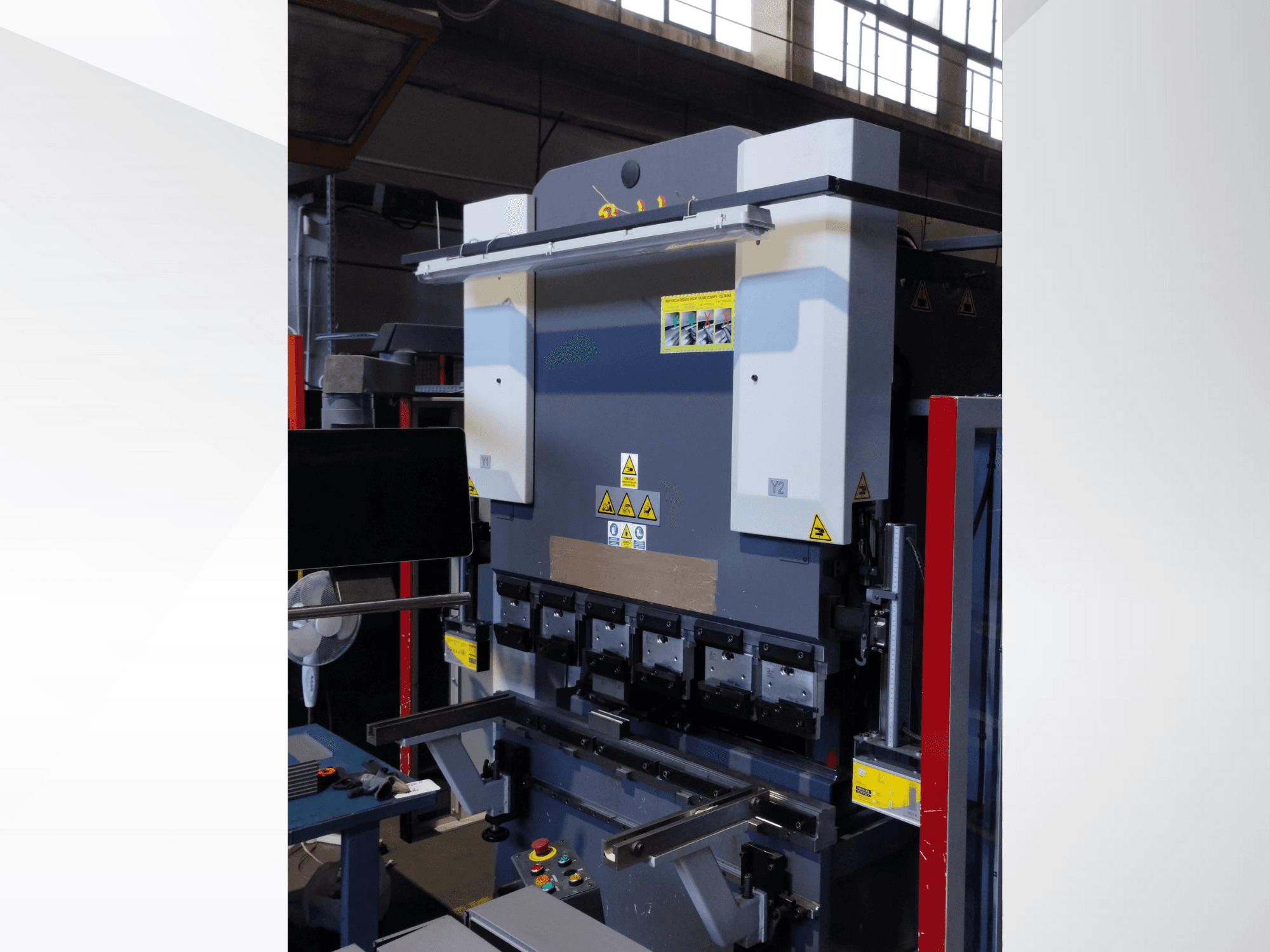 Abkant pres makinesi, önden görünüm. Görünür kontroller, güvenlik etiketleri ve hassas bükme için çoklu kalıp tutuculara sahiptir.