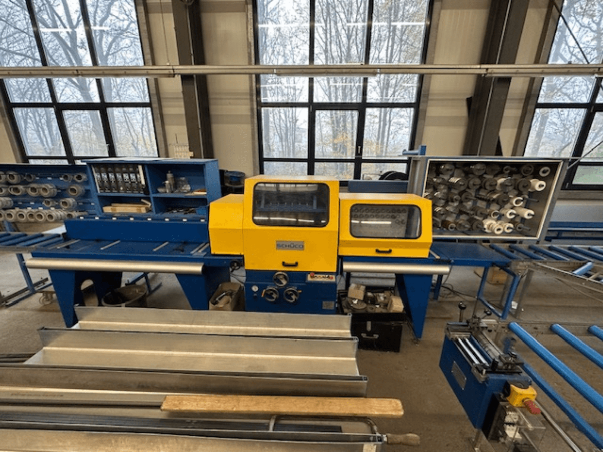 SCHÜCO ISOMAT 4 takım tezgahının önden görünümü, sarı bir kontrol paneli, çoklu silindirler ve bir saklama bölmesi içerir.