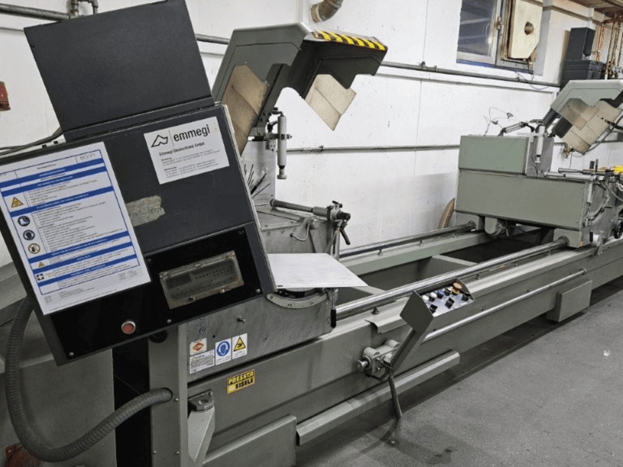 Emmegi endüstriyel kesim makinesi, önden görünüm, kontrol paneli, güvenlik etiketleri ve çalışma bileşenleri.