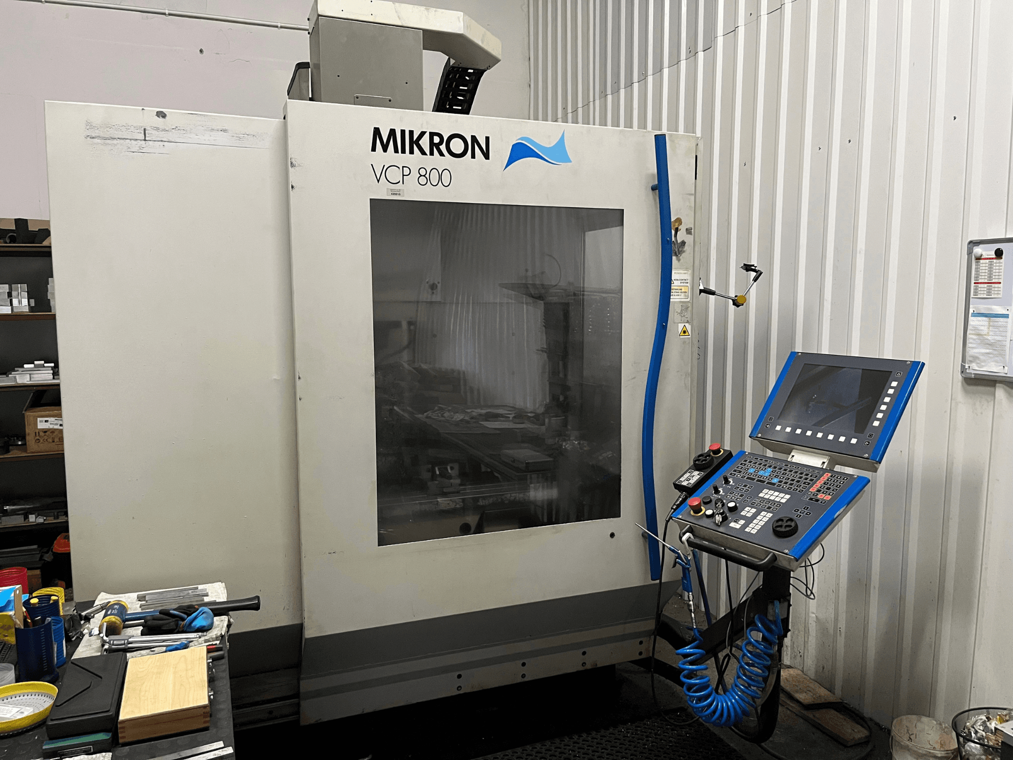 MIKRON VCP 800 dikey işleme merkezi, önden görünüm; ön planda bir çalışma tezgahı üzerinde kontrol paneli ve aletler yer almaktadır.