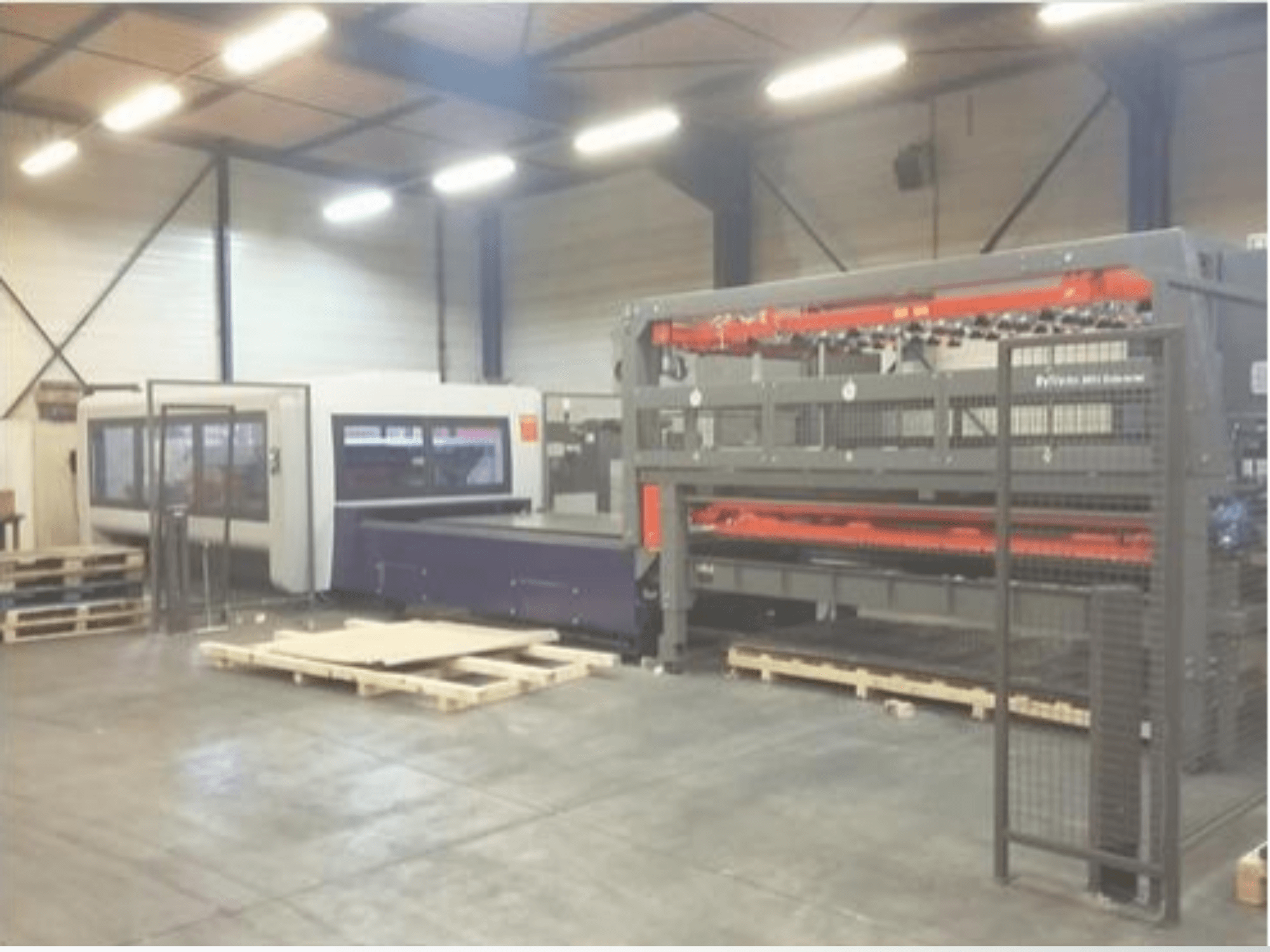 Bir depoda endüstriyel makine kurulumu; gri bir lazer kesici ve mor bir CNC yönlendirici içerir, paletlerle önden görünüm.