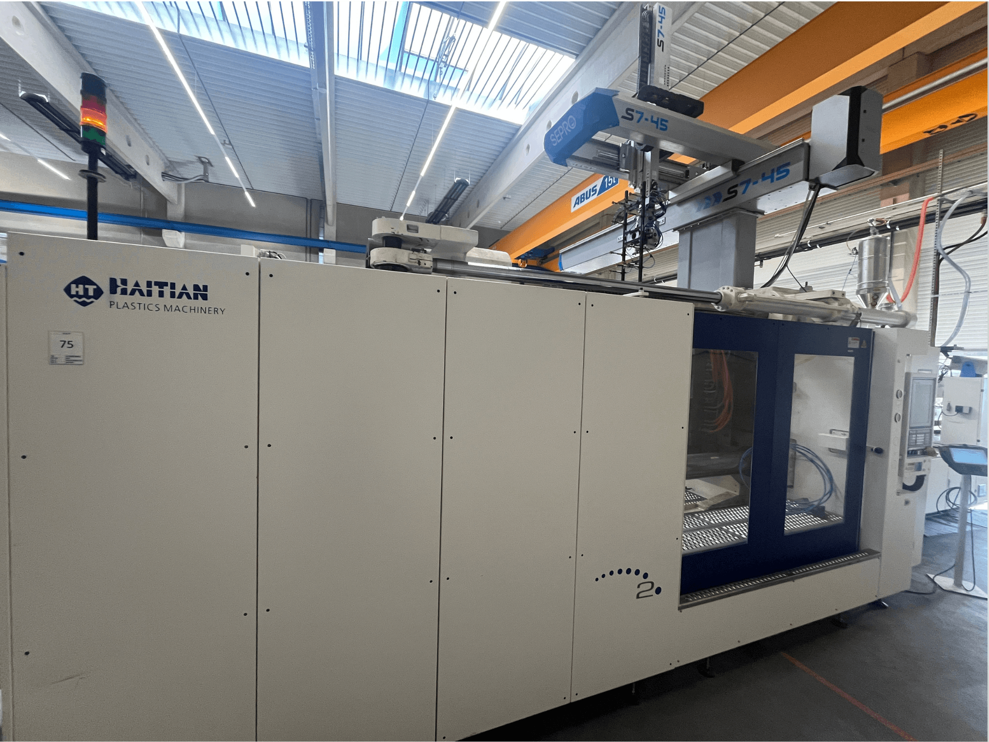 Kontrol paneli ve güvenlik ışığı göstergesi ile yandan görünümde Haiti S7-45 enjeksiyon kalıplama makinesi. Beyaz ve mavi tasarım.