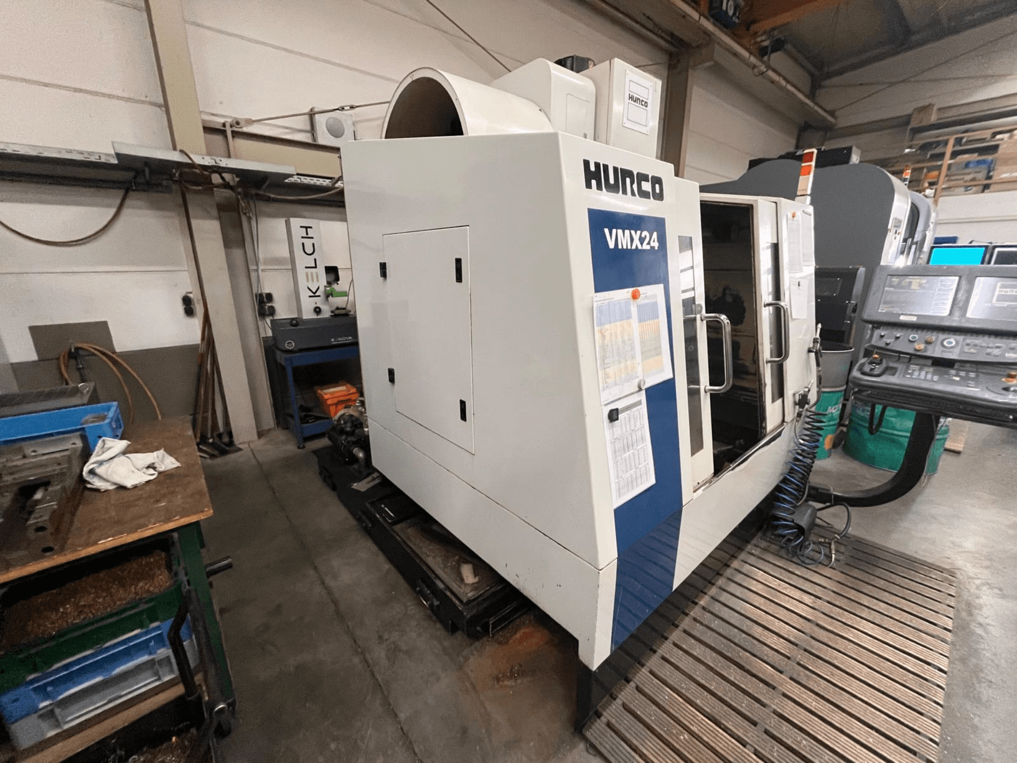 Hurco VMX24 CNC makinesi bir atölyede, önden görünüm; bir kontrol paneli ve açık erişim kapısına sahiptir.