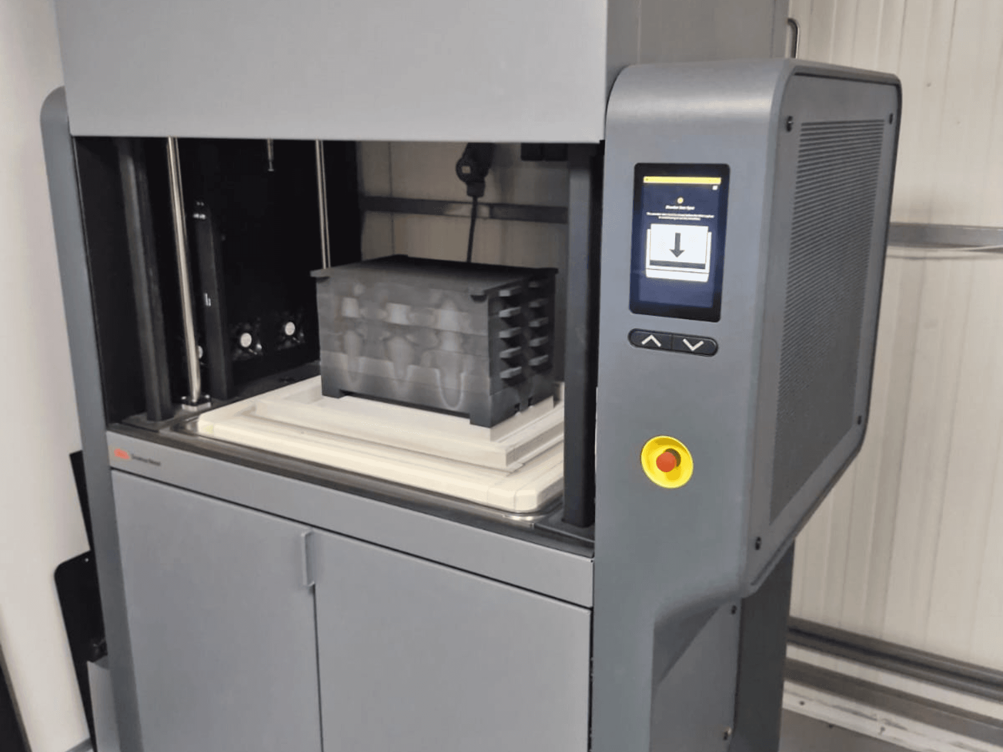 Desktop Metal'in Metal Studio 2 3D yazıcısı, kontrol panelini ve siyah konteynerli baskı yatağını gösteren önden görünüm.