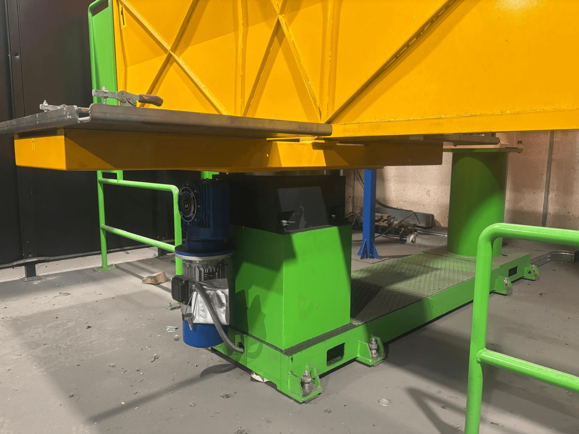 Yeşil ve sarı renkli endüstriyel makinelerin alçak önden görünümü, bir motor ve dokulu bir yüzeye sahip platform.