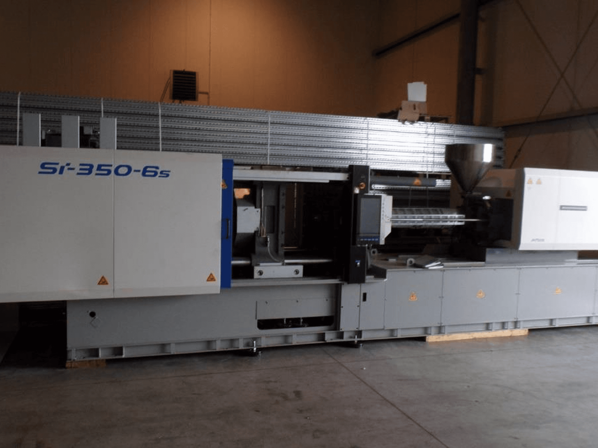 Yan görünümde Si-350-6s enjeksiyon kalıplama makinesi, geniş bir endüstriyel ortamda bulunan bir hazne ve kontrol paneline sahiptir.
