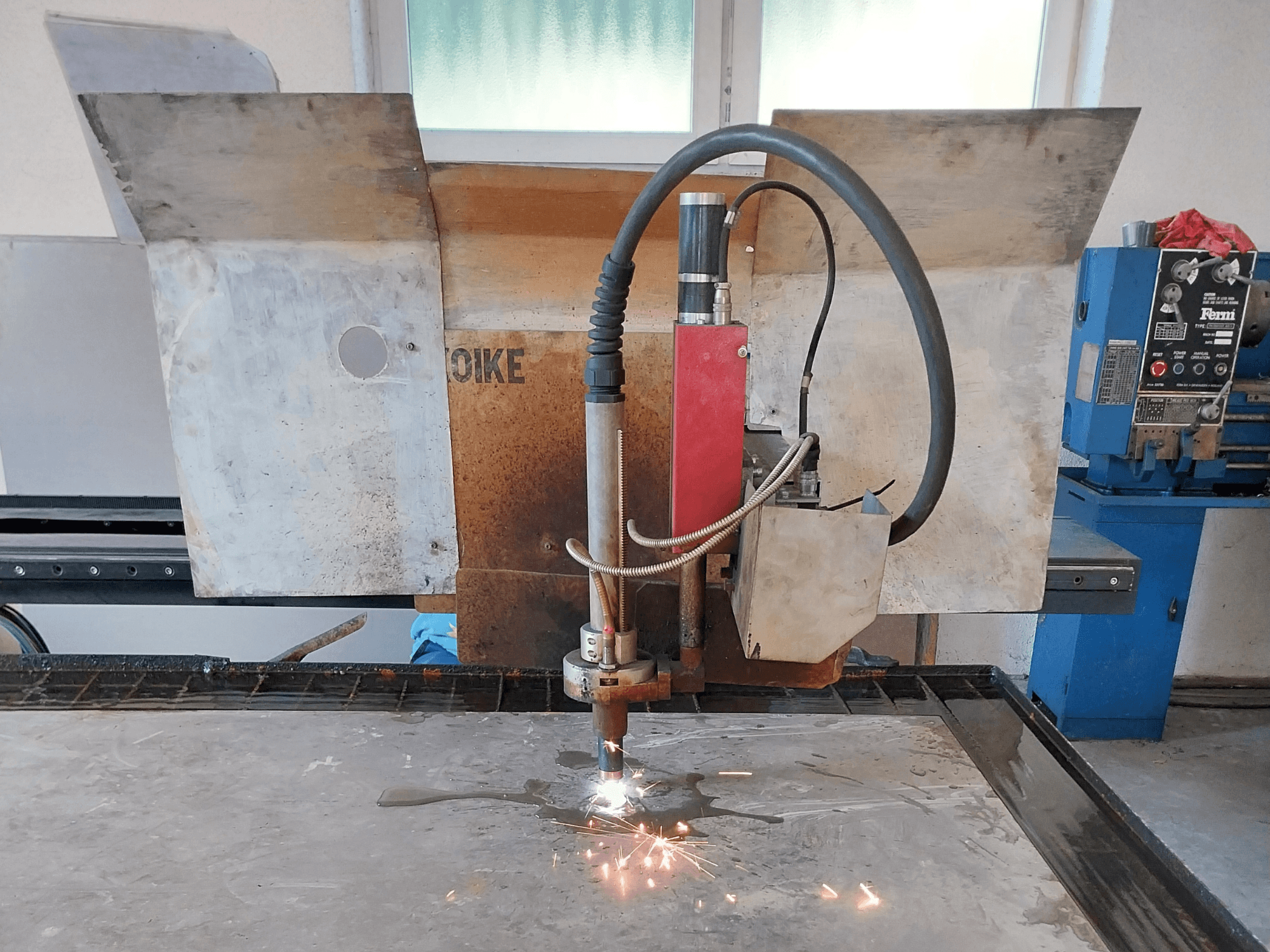 Bir çalışma masasındaki metal bir yüzeyin üzerine yerleştirilmiş, kıvılcımların uçuştuğu bir Oike plazma kesicinin önden görünümü.