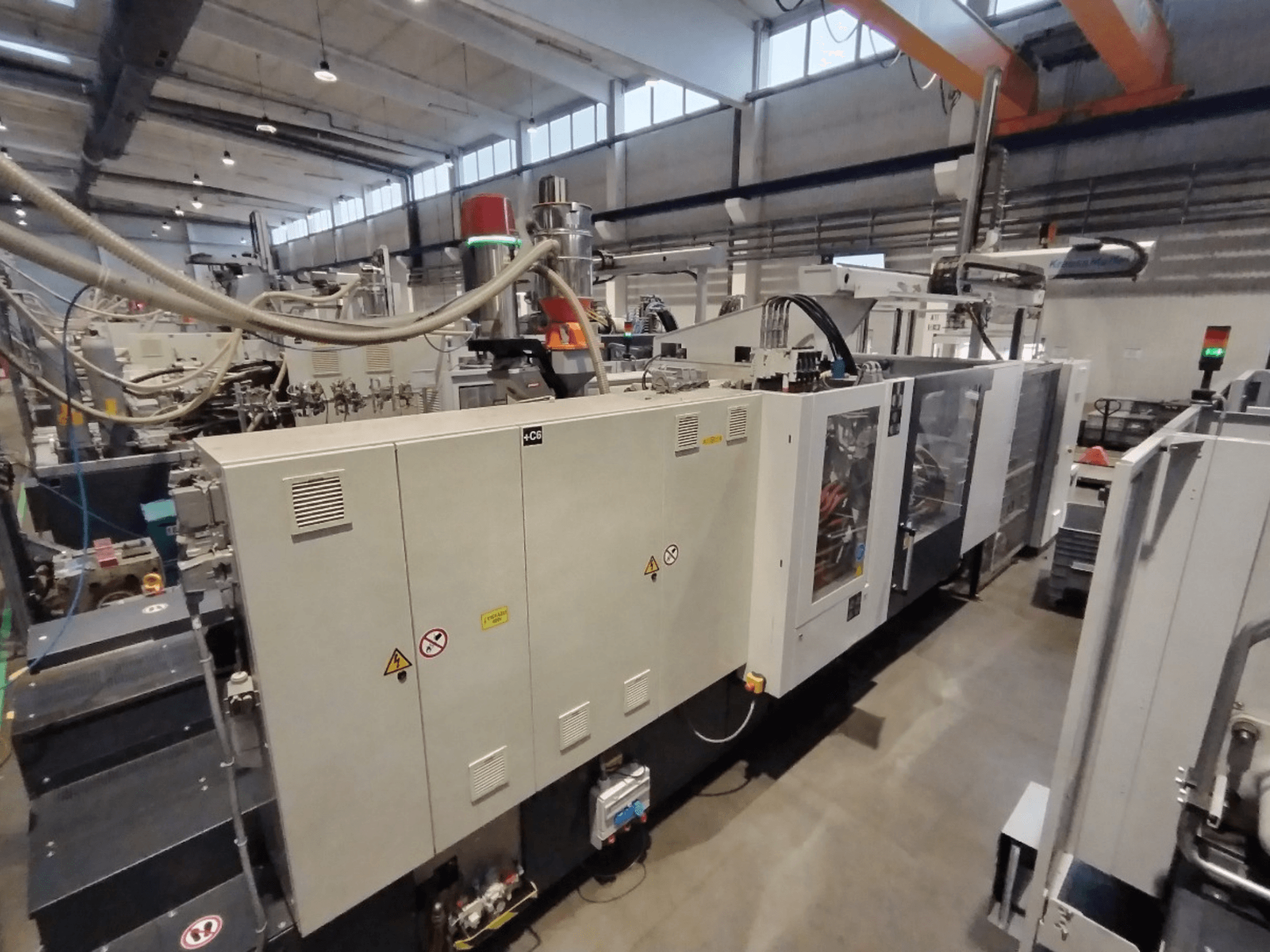 Kontrol paneli ve güvenlik uyarıları ile yandan gösterilen endüstriyel enjeksiyon kalıplama makinesi. Marka: Bilinmiyor.