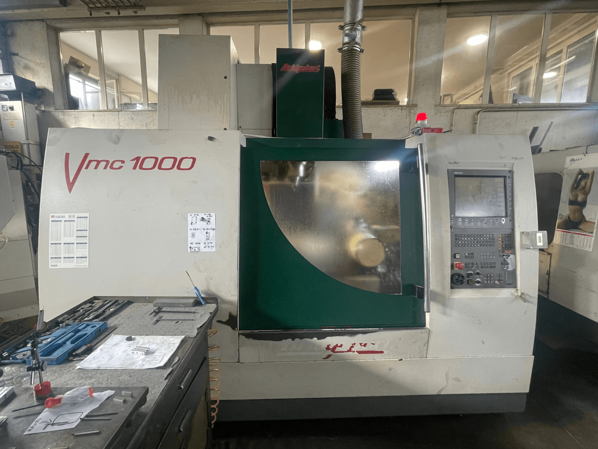 Bridgeport VMC 1000/30 dikey işleme merkezi, önden görünüm; kontrol paneli ve ana gövde gösterilmekte olup, yanında takımlar bulunmaktadır.