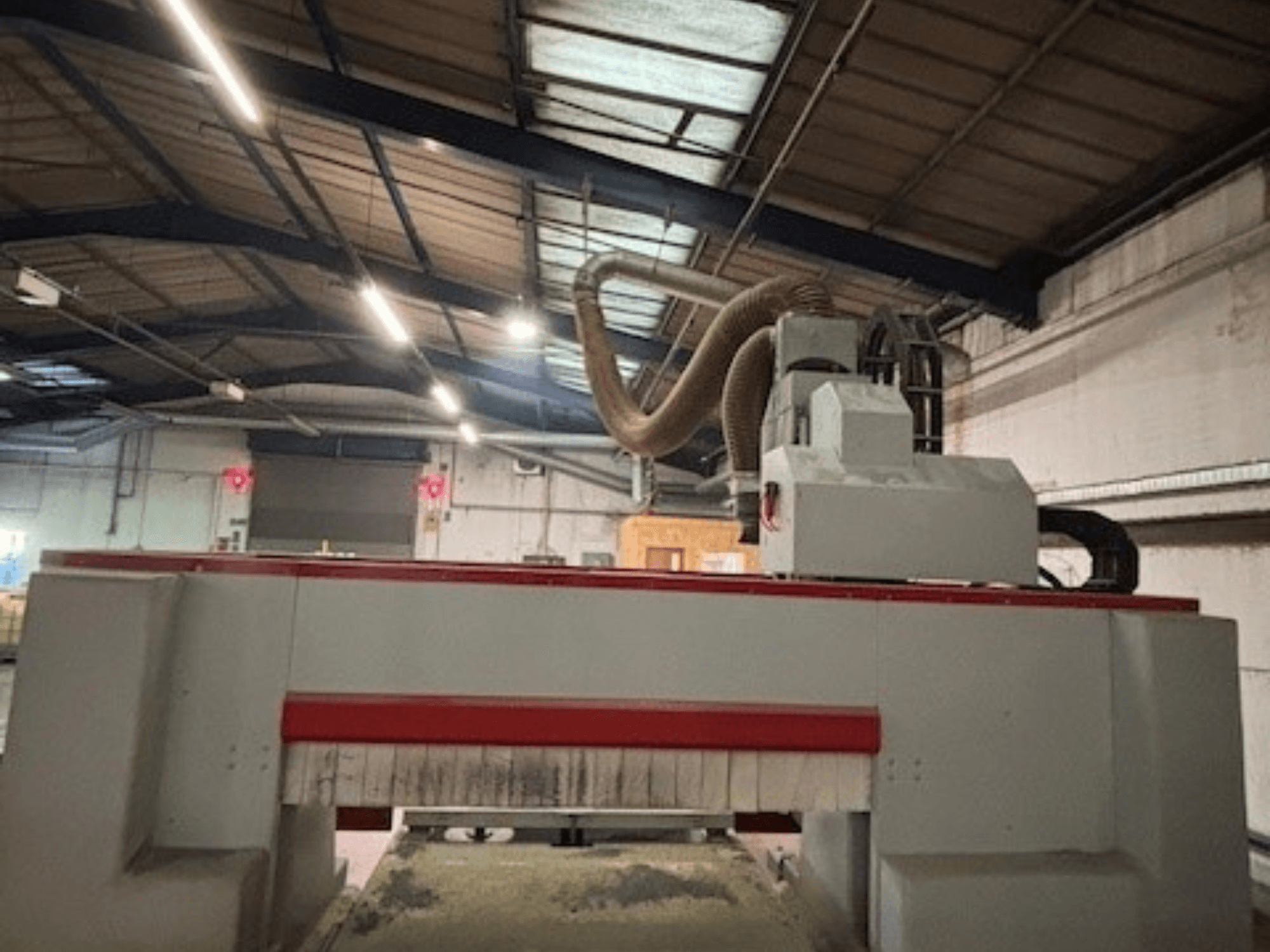 Bir atölyede CNC router makinesi, kırmızı ve gri tasarımı vurgulayan yandan görünüm, toz emme sistemi takılı.