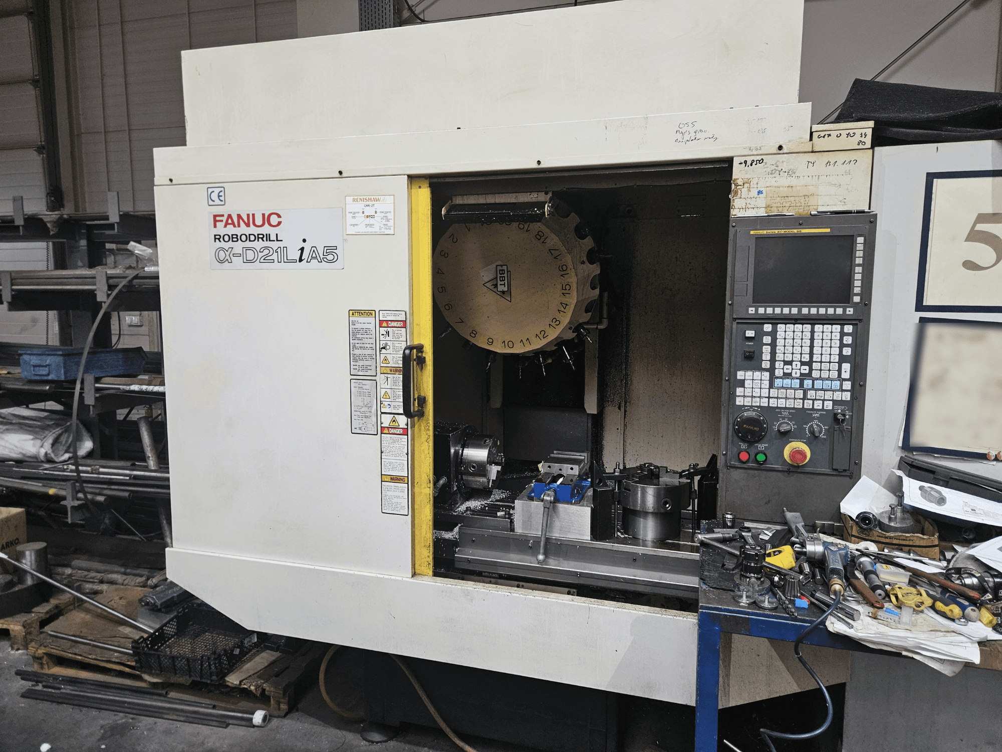 FANUC Robodrill α-D21LiA5, takım tutucu ve kontrol panelini gösteren önden görünüm, bir atölyede takımlar ve ekipmanlarla çevrelenmiştir.