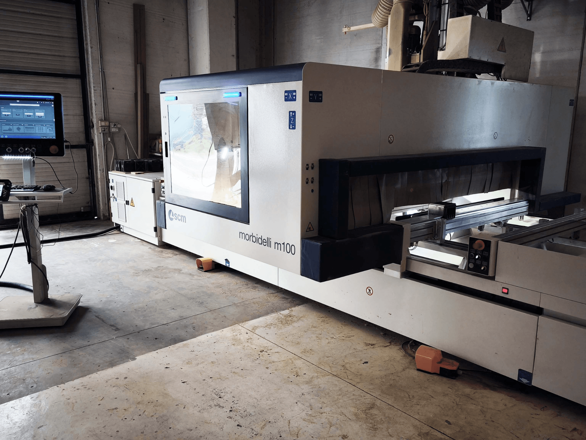 SCM Morbidelli M 100 CNC ahşap işleme merkezinin yandan görünümü; kontrol paneli, çalışma alanı ve güvenlik özellikleri gösterilmektedir.