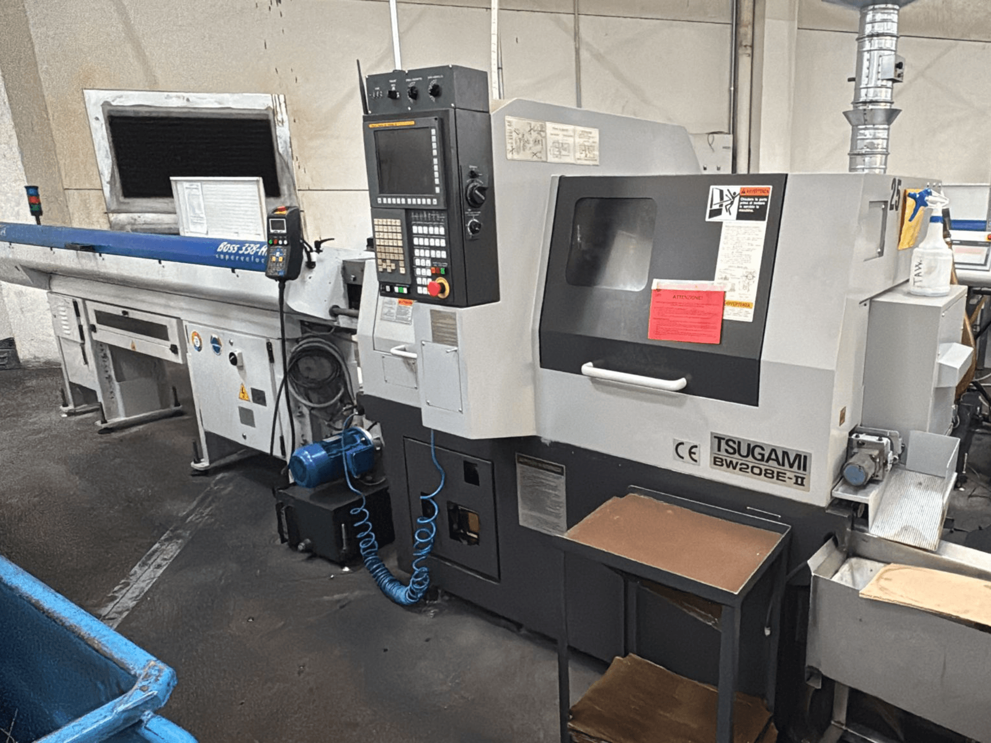 Bir atölyedeki Tsugami BW208E-II CNC makinesi, ön açıdan gösterilmiş, kontrol paneli ve güvenlik etiketleri görülebilir.